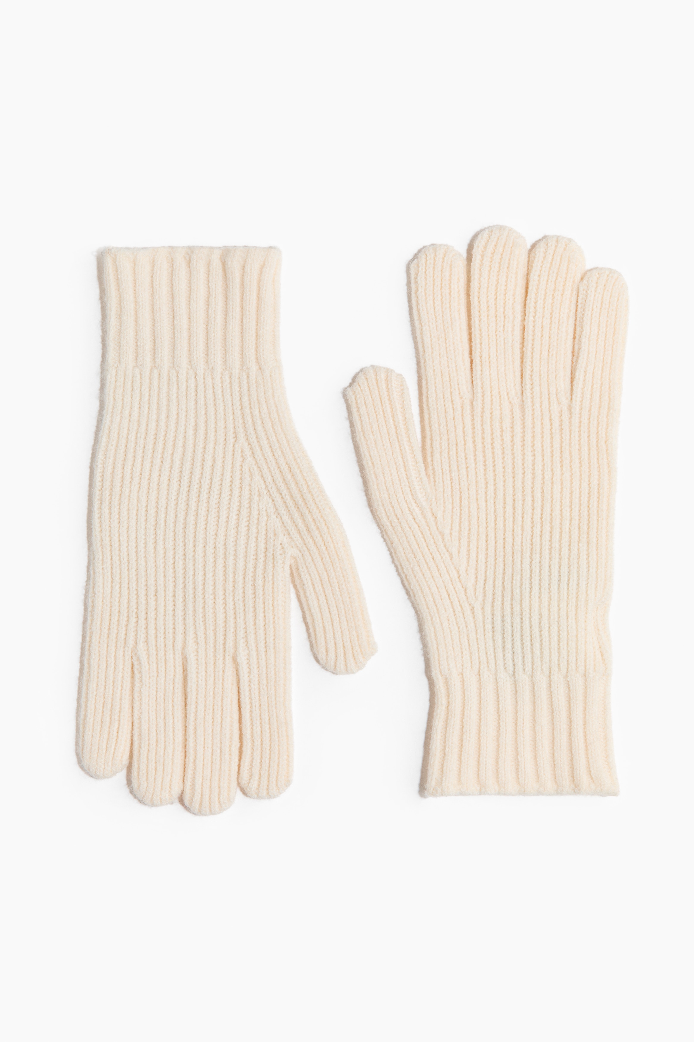 Gloves in a soft, off-white fine knit with ribbed cuffs are being worn by the model, who is touching the fingers of one glove with their other hand. The gloves are styled with a matching cream-coloured knit sweater.