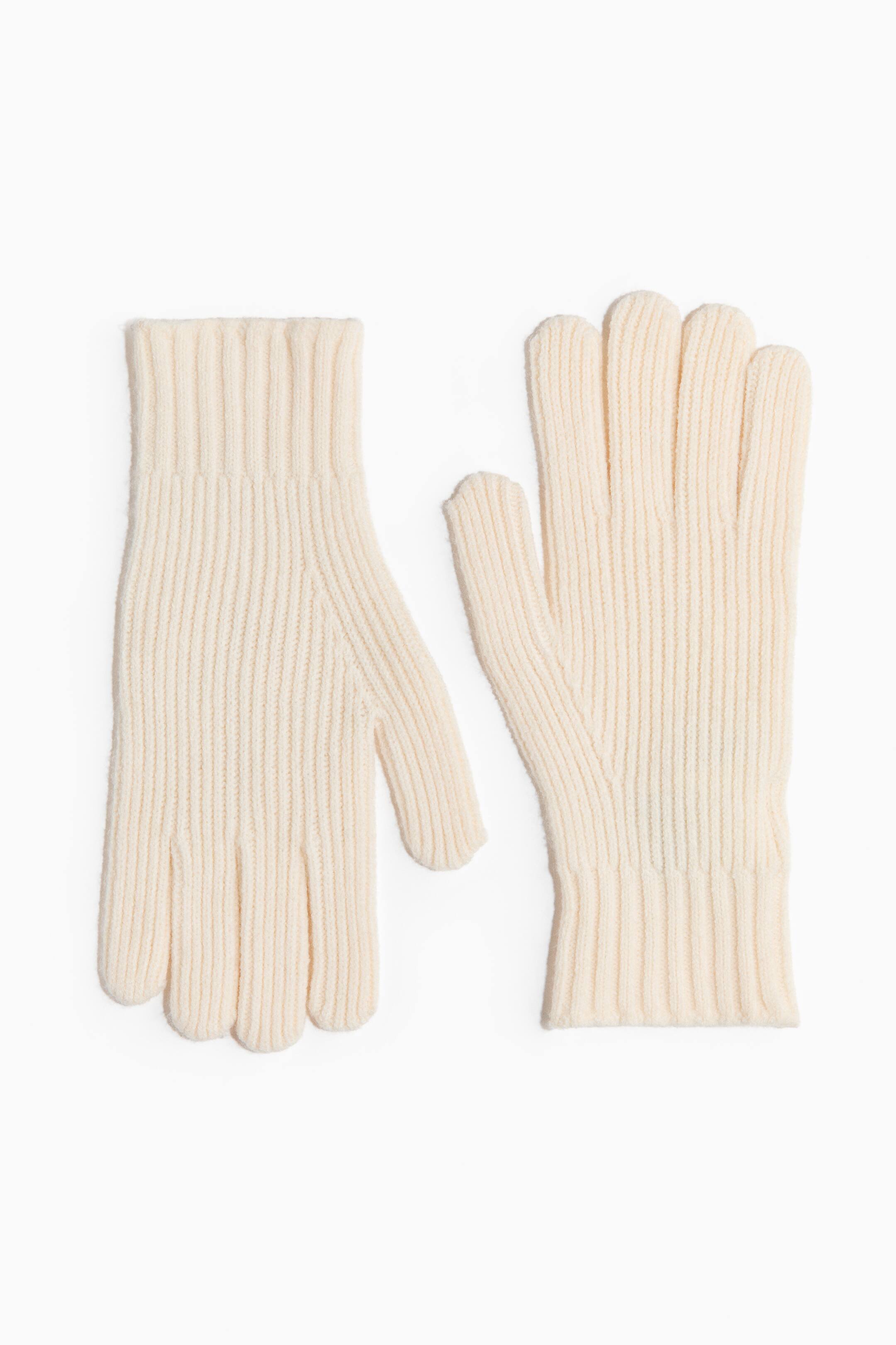 View larger image: A pair of cream-coloured knit gloves is lying flat, featuring full fingers and ribbed cuffs. Both gloves display a prominent ribbed pattern throughout, with one glove showing its backhand and the other its palm.