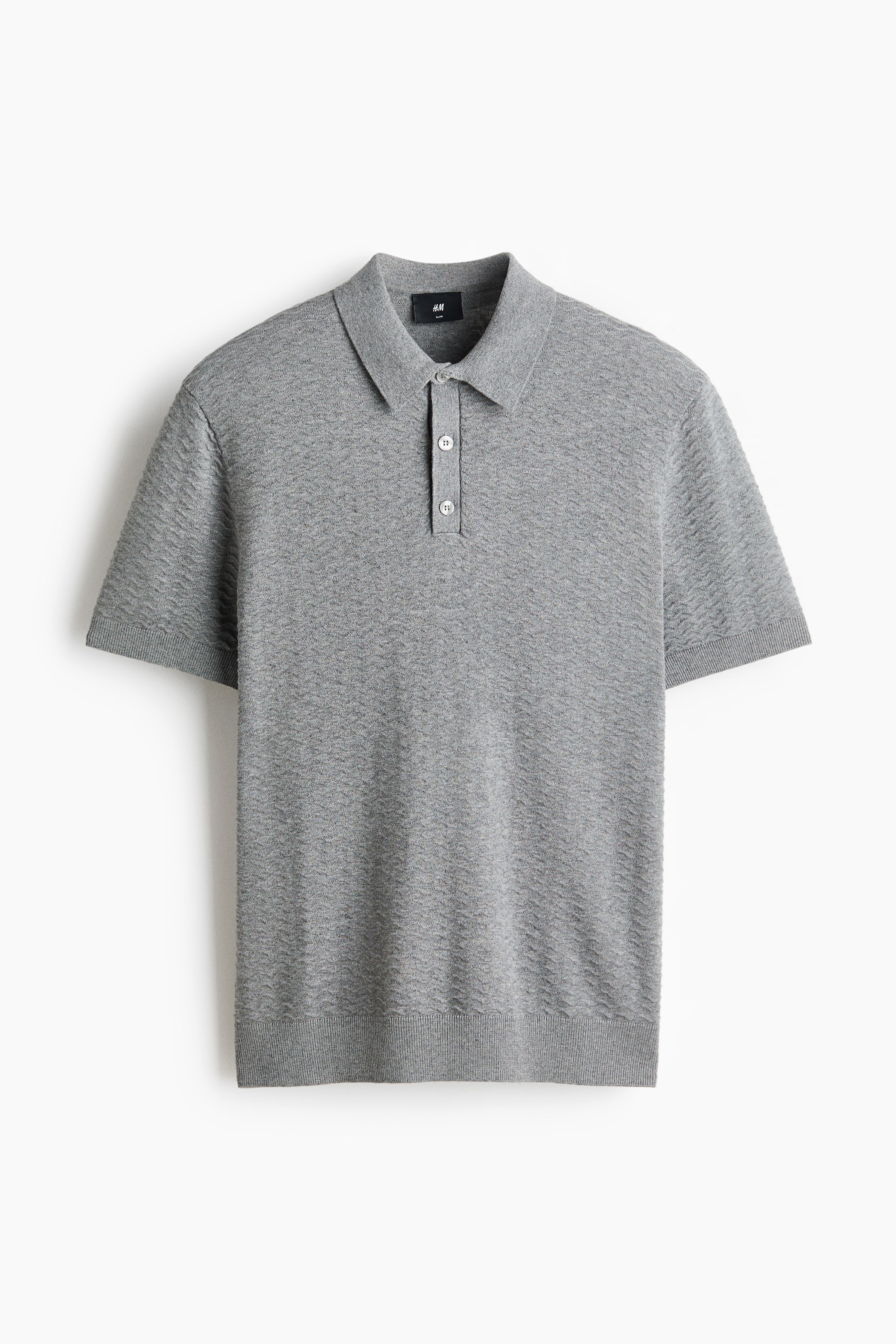 Ampliar la imagen: Una camisa polo tejida en color gris se muestra de frente, con un sutil tejido de zig-zag a lo largo de su cuerpo y mangas cortas. Incluye un cuello, una tapeta de dos botones y puños y dobladillo acanalados, presentando una silueta ajustada y entallada.