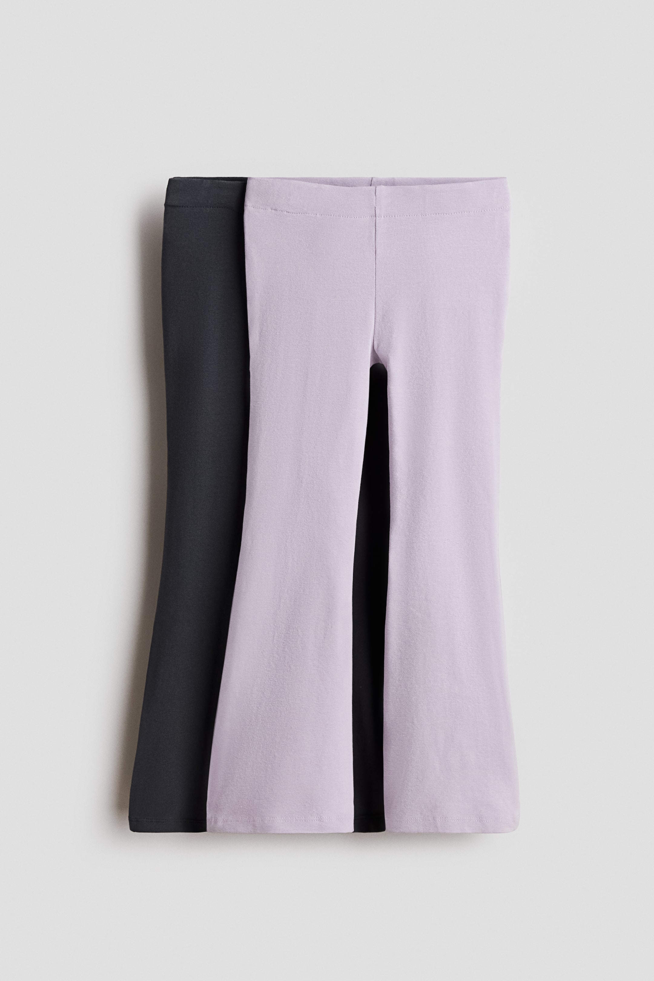 View larger image: Two pairs of leggings are presenting from the FRONT, one in dark gray and one in light purple. Each pair is featuring an elasticated waist and flared legs, and is made from a soft cotton jersey.
