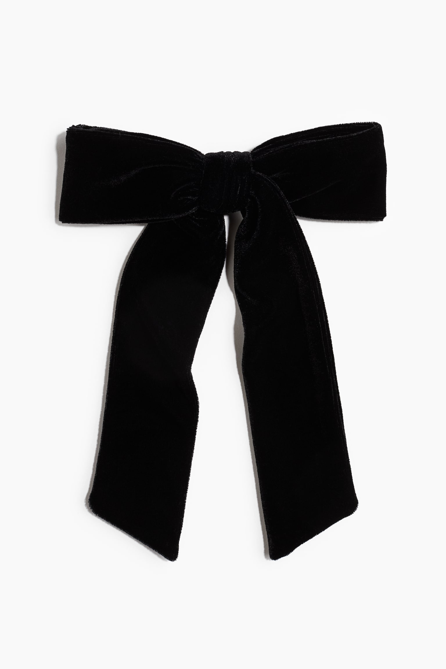 A metal hair clip is presenting a front view of a large black velvet bow with a central knot and two structured loops. Two wide, flat tails hang downward from the knot, showcasing the soft, plush texture of the fabric.