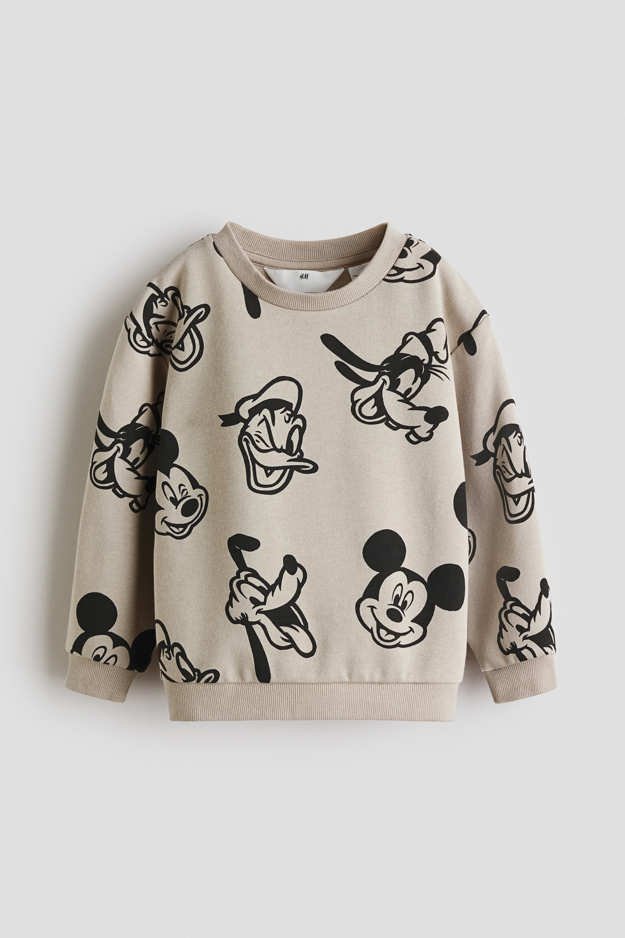 Se større billede: Den beige sweatshirt har et all-over print med sorte Disney-figurer, herunder Mickey Mouse, Anders And og Fedtmule. Den er designet med en ribbet rund hals, ribbede manchetter og en ribbet kant.