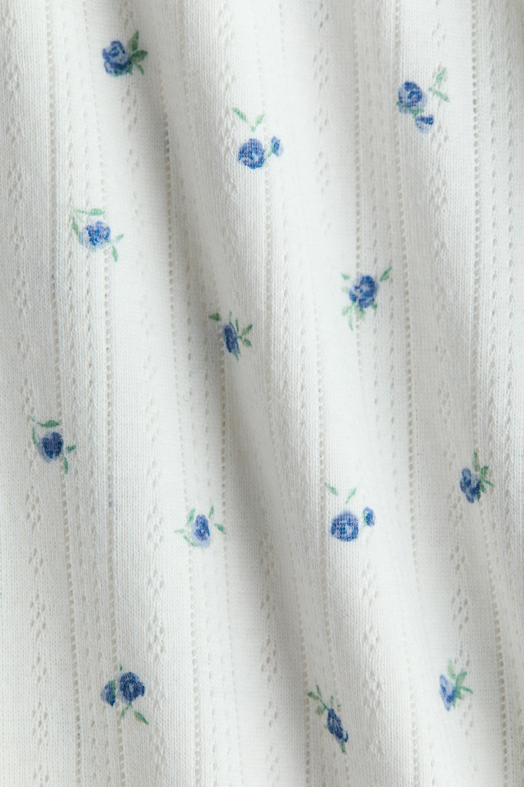 Agrandir l'image: Le bas de pyjama met en avant un tissu en jersey pointelle de coton blanc doux. Ce tissu présente un motif de petites fleurs bleues et des rangées verticales de détails ajourés.