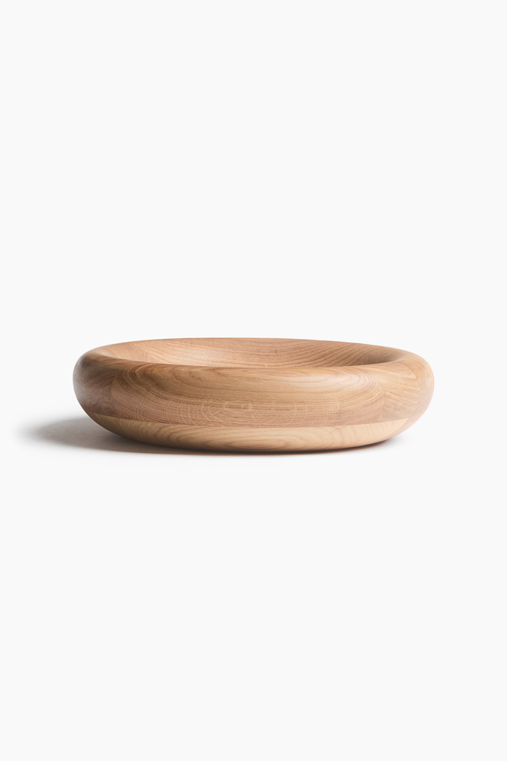 View larger image: A shallow wooden bowl is shown from the front, featuring a thick, rounded rim and a smooth, curved outer profile. The bowl displays a natural, light-coloured wood grain pattern that wraps horizontally around its circular shape.