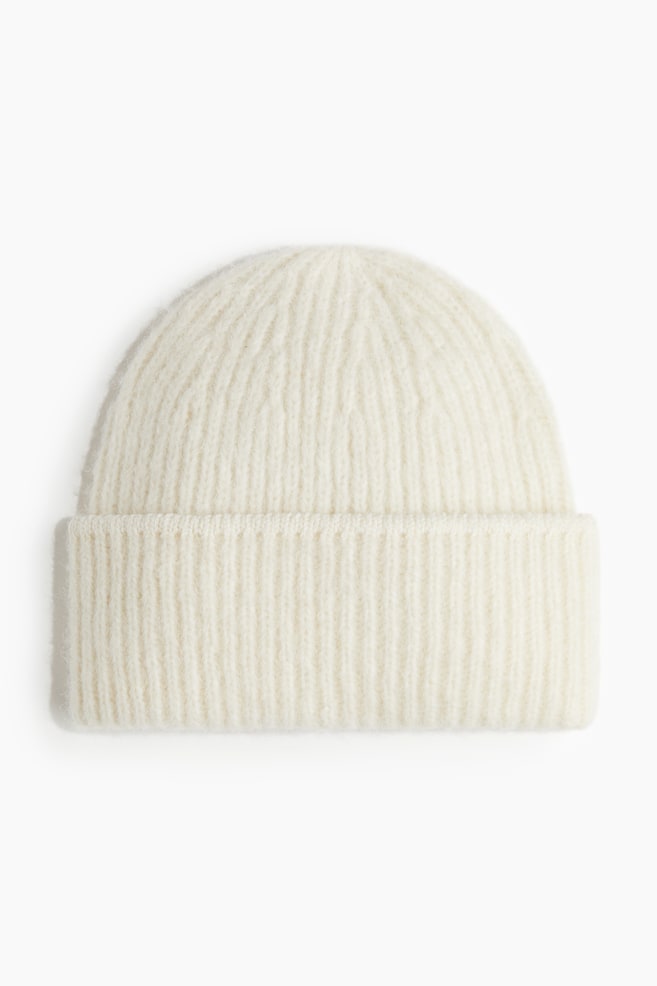 A white beanie is being presented from the front. It is displaying a ribbed knit pattern throughout its rounded crown and folded brim. - 1