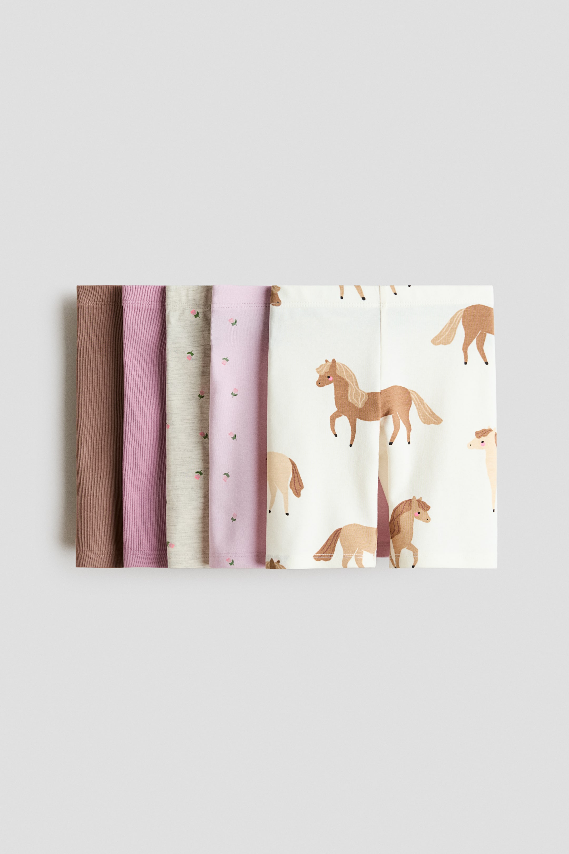 Agrandir l'image: Cinq paires de leggings pour bébé sont empilées, montrant leurs sections inférieures, avec les deux premières paires côtelées en marron et violet. Les paires restantes incluent un gris chiné clair et un violet clair avec de petits motifs floraux roses, ainsi qu'une paire blanc cassé arborant un motif répétitif de chevaux marron dessinés.