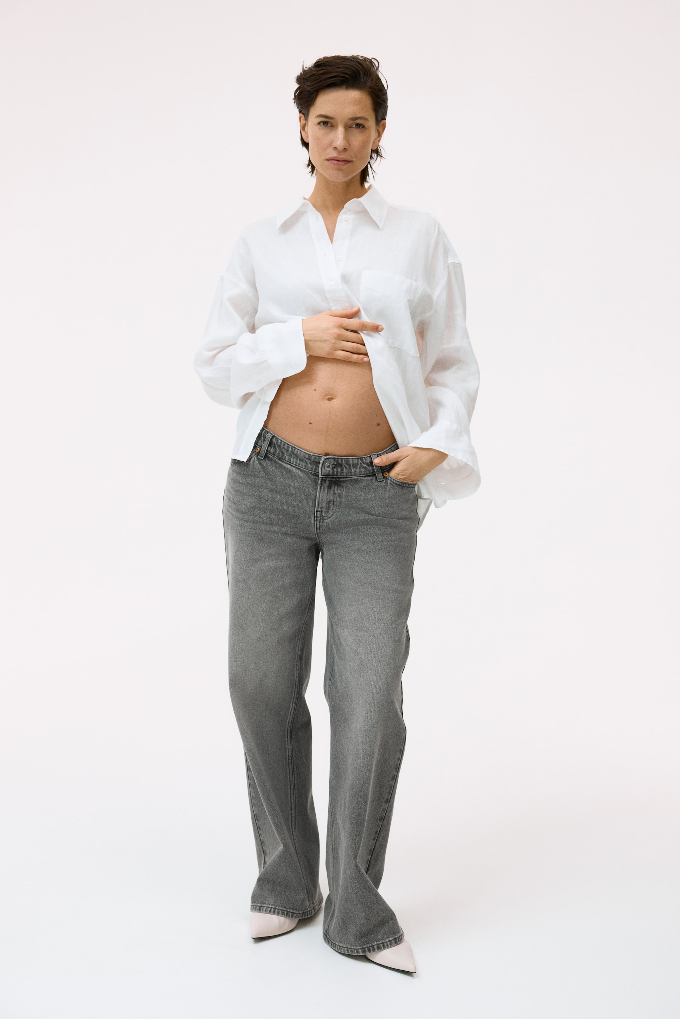 View larger image: Grey washed jeans showcase a relaxed, straight-leg fit that extends over the tops of the shoes. They feature a low-rise waistband with visible buttons and belt loops, presented from a front-facing angle.