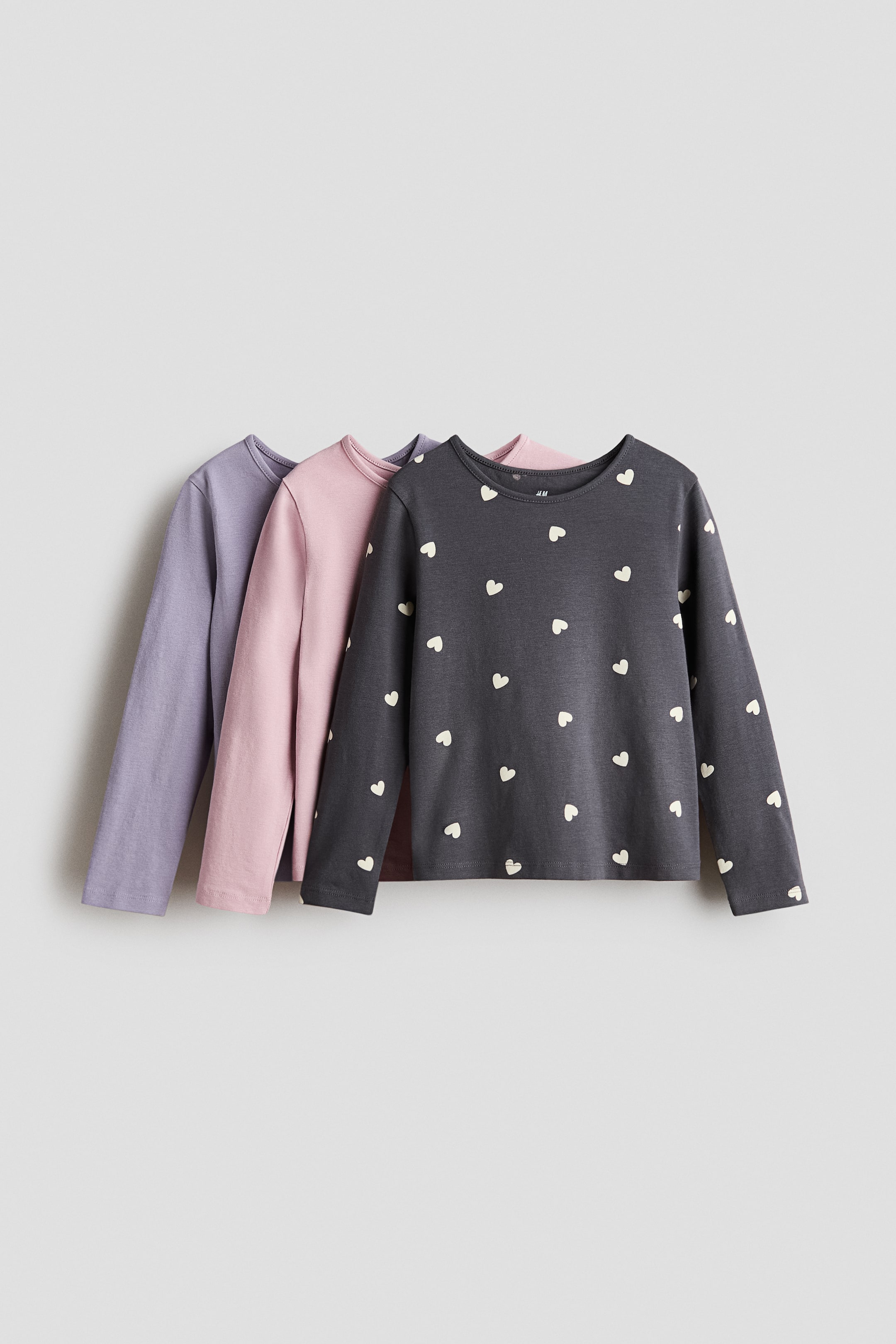 View larger image: Three long-sleeve cotton jersey tops are layered and facing forward, featuring a round neckline with narrow trim. The front top is charcoal grey with an all-over print of small white hearts, while the middle top is solid light pink and the back top is solid light purple.