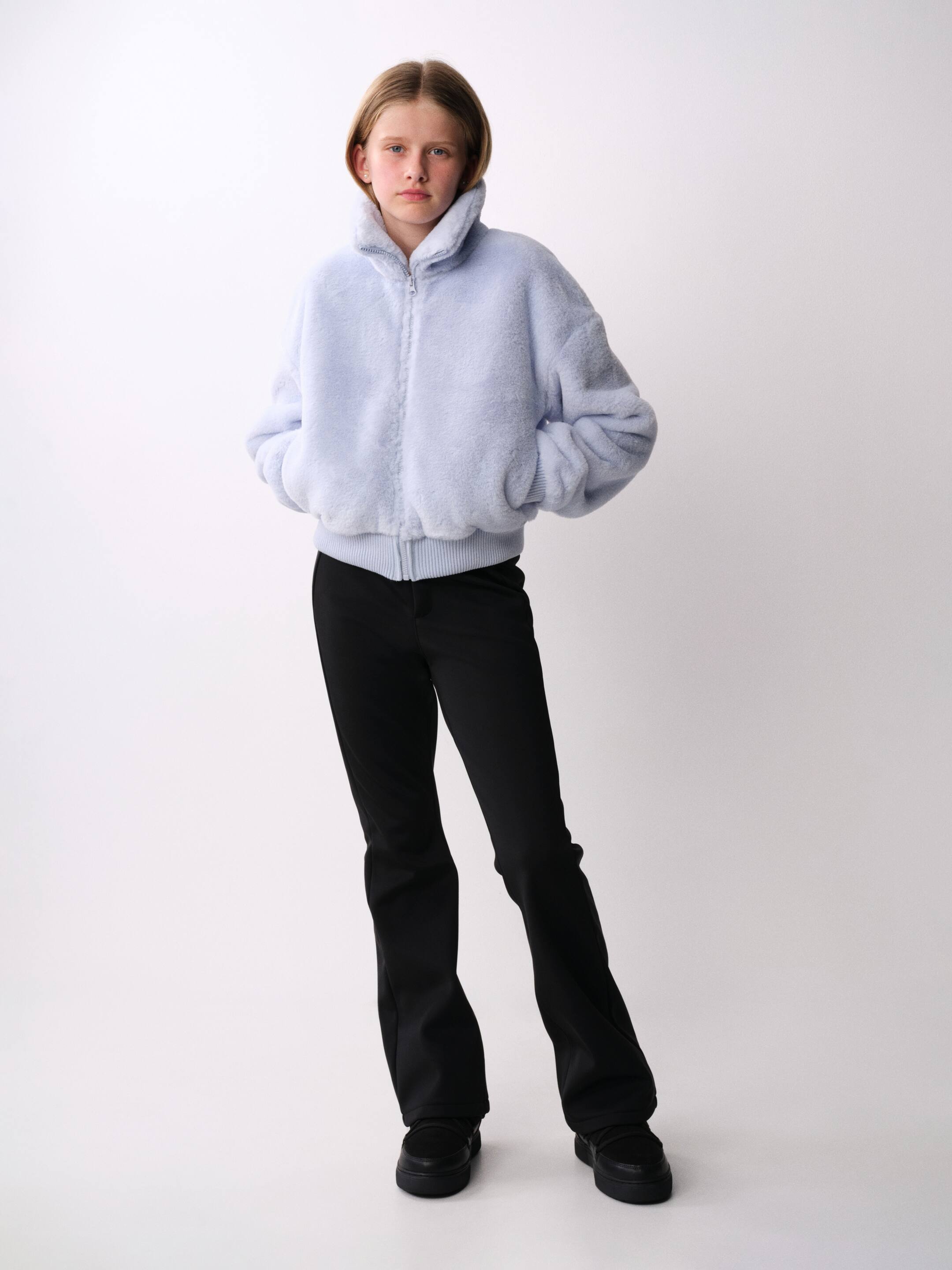 Visualizza immagine più grande: I pantaloni da sci neri in softshell sono mostrati da un’angolazione frontale, con una vestibilità slim sulle cosce e gambe svasate, caratterizzati da cuciture flatlock verticali sul davanti. I pantaloni a vita alta sono abbinati a una giacca morbida azzurra con zip e a scarpe nere con suola spessa.