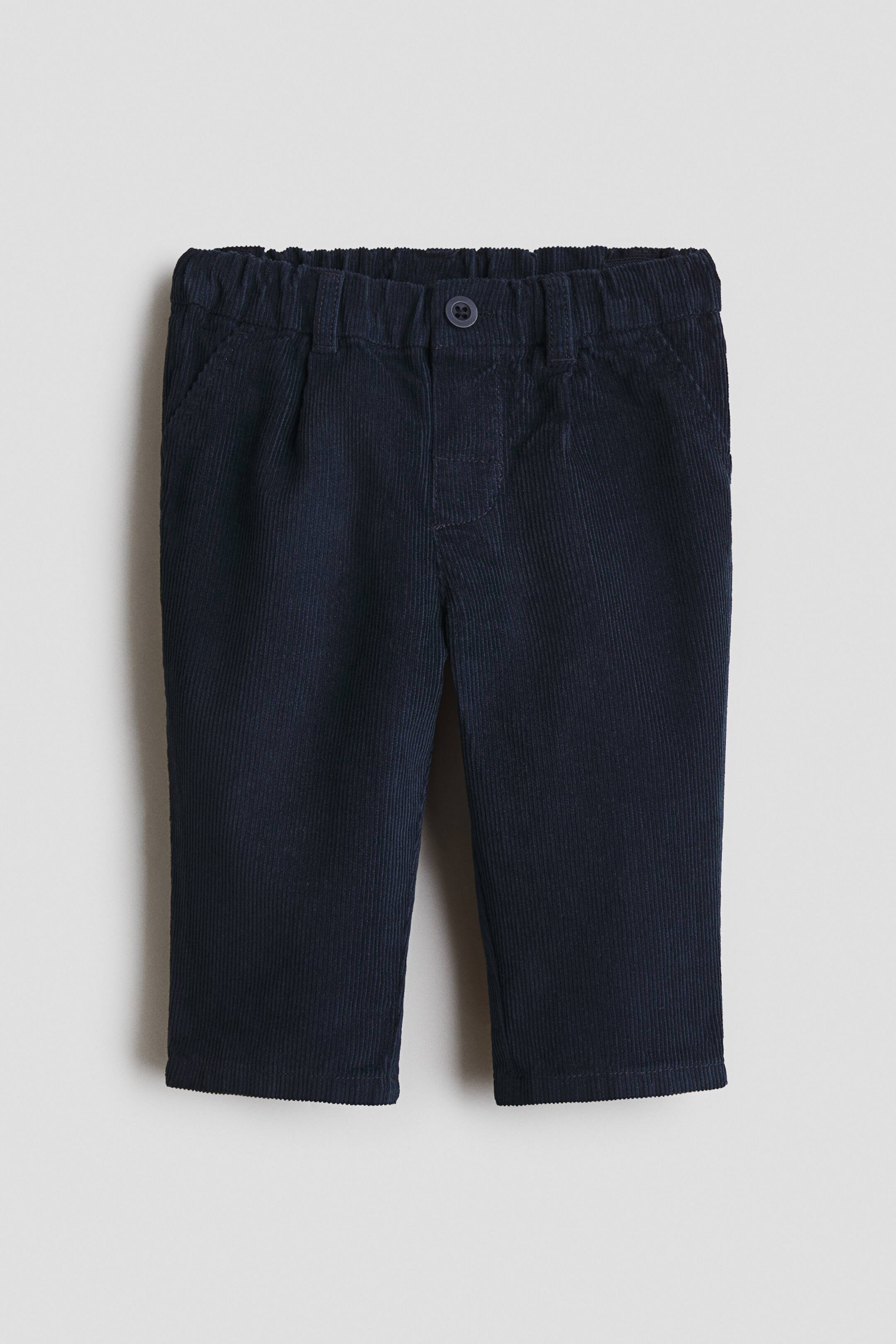 Grotere afbeelding bekijken: De donkerblauwe corduroy broek heeft een elastische tailleband met riemlussen en een enkele knoopsluiting aan de voorkant. Aan de voorkant zijn twee schuine zakken zichtbaar, en de broekspijpen lopen recht.