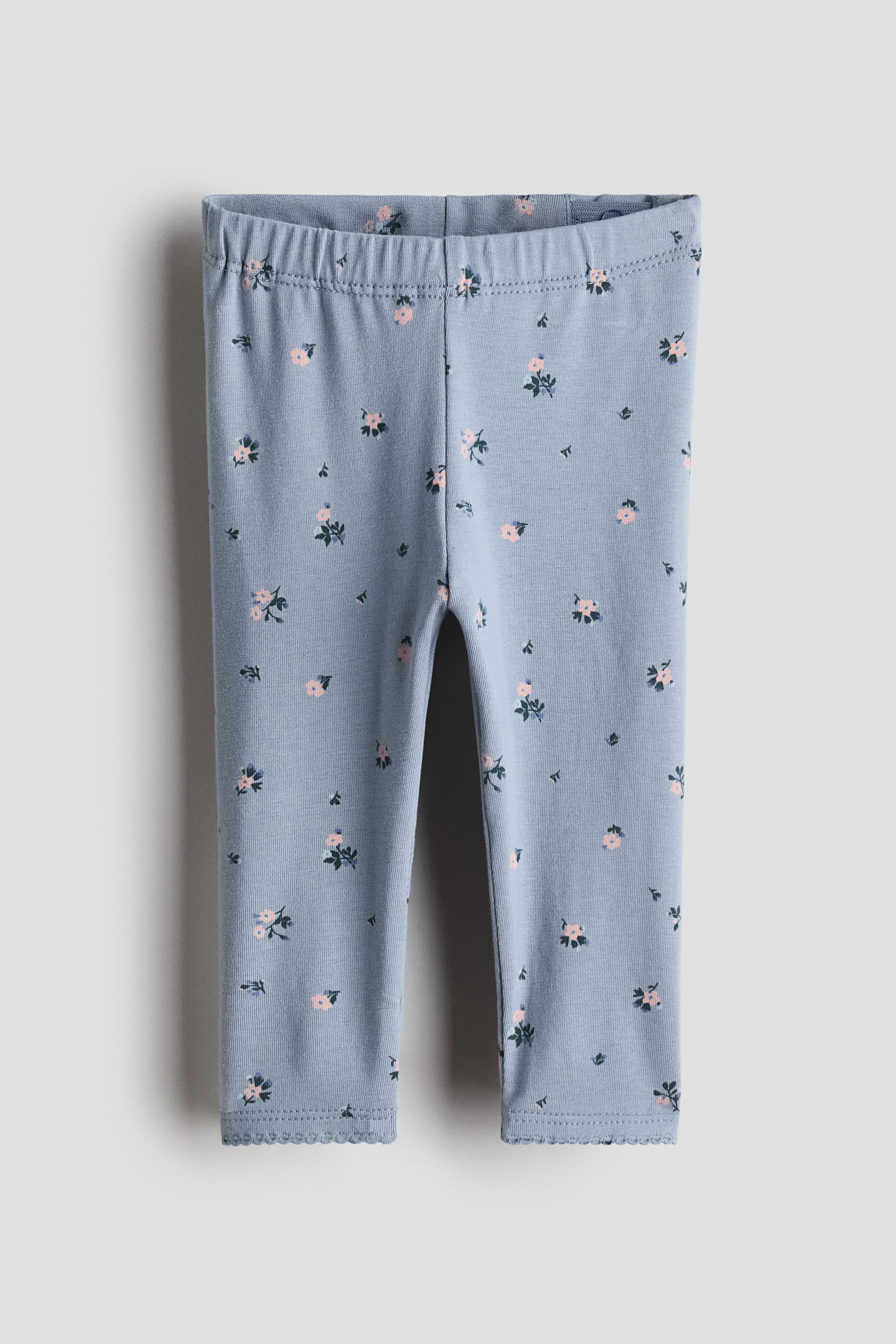 Voir une image plus grande: Les leggings présentent un tissu en jersey de coton doux bleu clair avec un imprimé intégral de petites fleurs roses et vertes, visibles de face. Ils sont dotés d'une taille élastique froncée et de poignets festonnés.