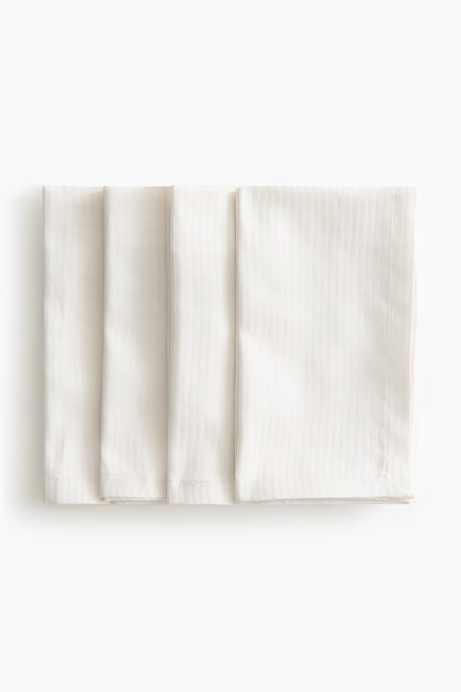 Four off-white fabric napkins are lying flat and overlapping in a neat row, facing front. Each folded napkin is displaying a rectangular shape with a subtle, vertical ribbed texture and stitched hems. - 1