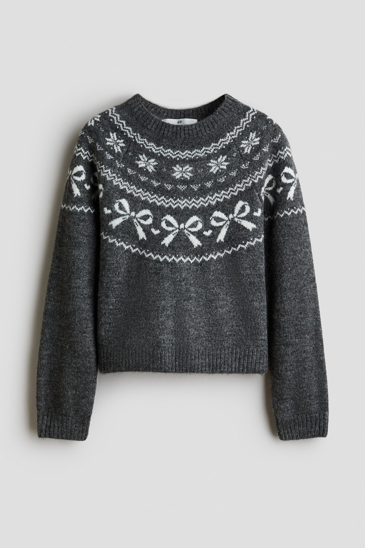 Un pull en maille gris foncÃ© prÃ©sente un empiÃ¨cement de style Fair Isle blanc avec des motifs de flocons de neige et de nÅuds, montrÃ© de face. Le vÃªtement affiche un col rond cÃ´telÃ©, des poignets cÃ´telÃ©s et un ourlet cÃ´telÃ©.