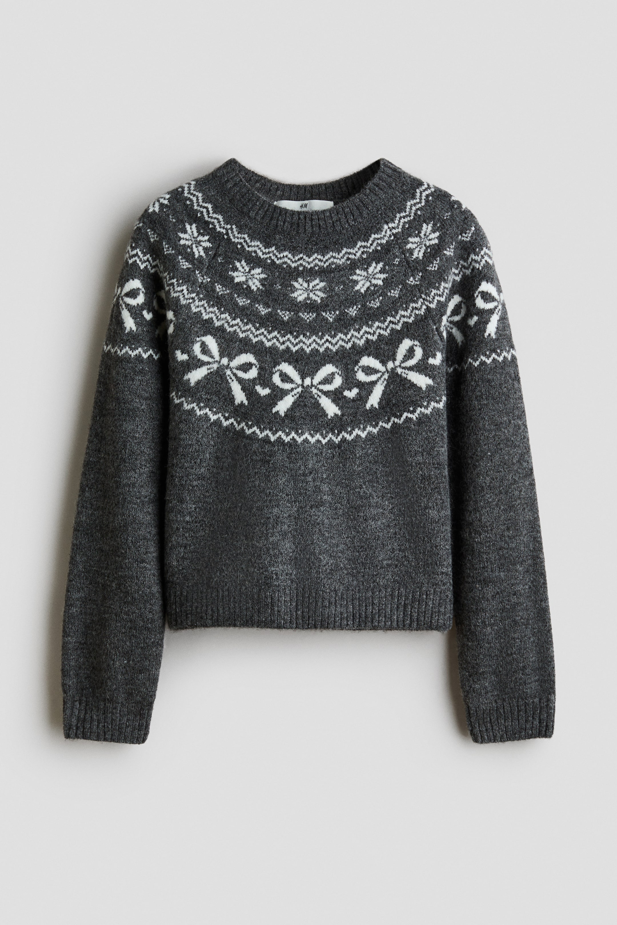 Agrandir l'image: Un pull en maille gris foncé présente un empiècement de style Fair Isle blanc avec des motifs de flocons de neige et de nœuds, montré de face. Le vêtement affiche un col rond côtelé, des poignets côtelés et un ourlet côtelé.