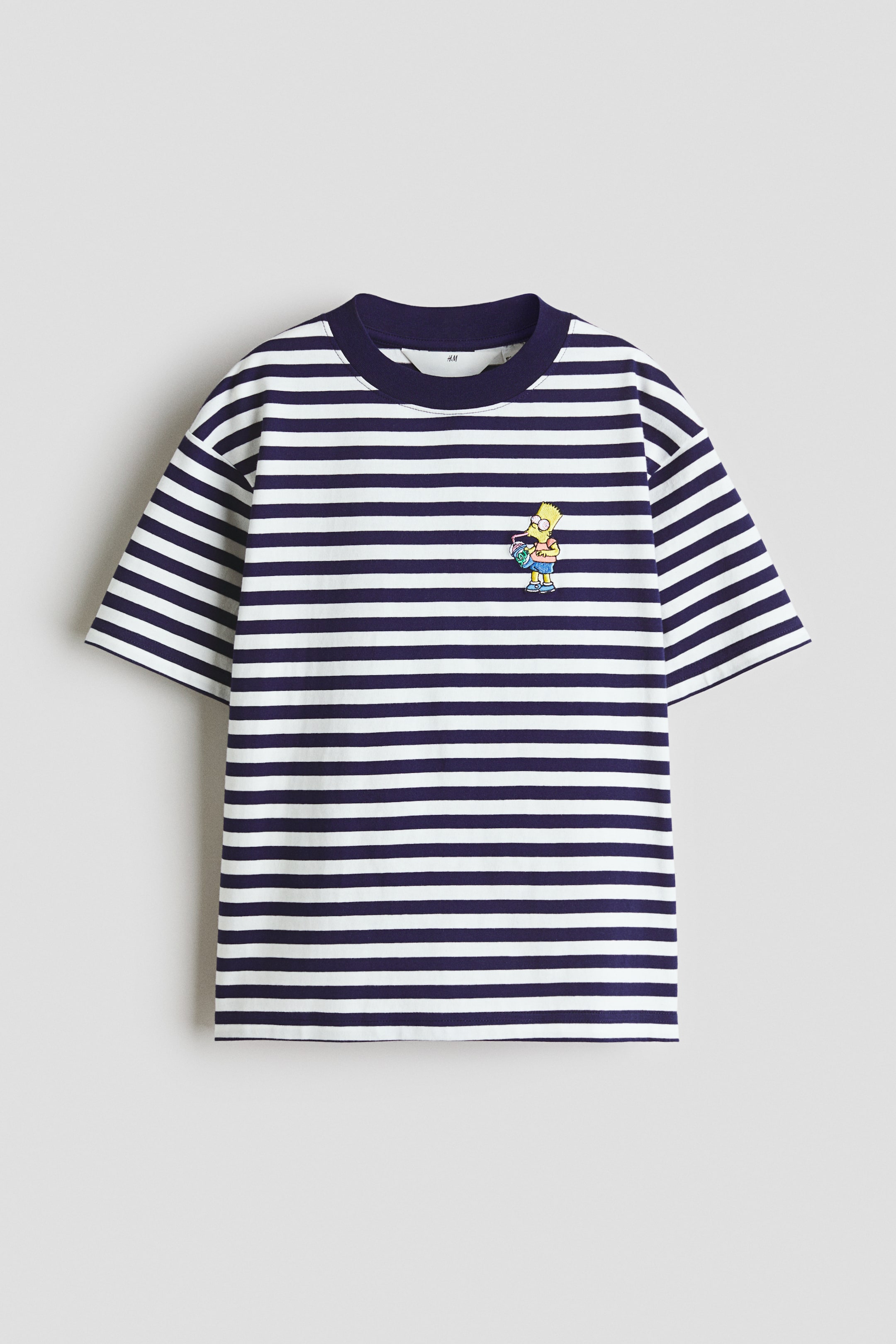Voir une image plus grande: Un t-shirt est présenté de face, arborant des rayures horizontales blanches et bleu marine. Une bordure côtelée bleu marine détaille l'encolure ronde, et un petit personnage de dessin animé jaune brodé apparaît sur la poitrine gauche, mettant en valeur une coupe ample avec des épaules tombantes.