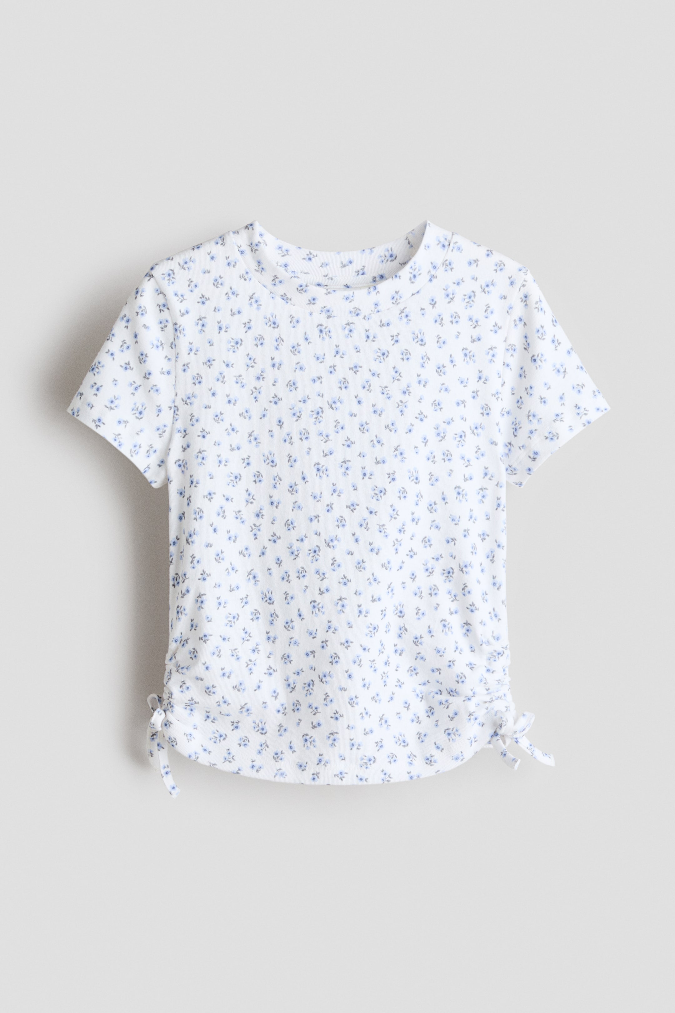 View larger image: A short-sleeve top in cotton jersey features a round neckline and a blue floral print all over a white background. Decorative drawstrings with sewn-in bows appear on each side of the hem, creating a ruched effect.