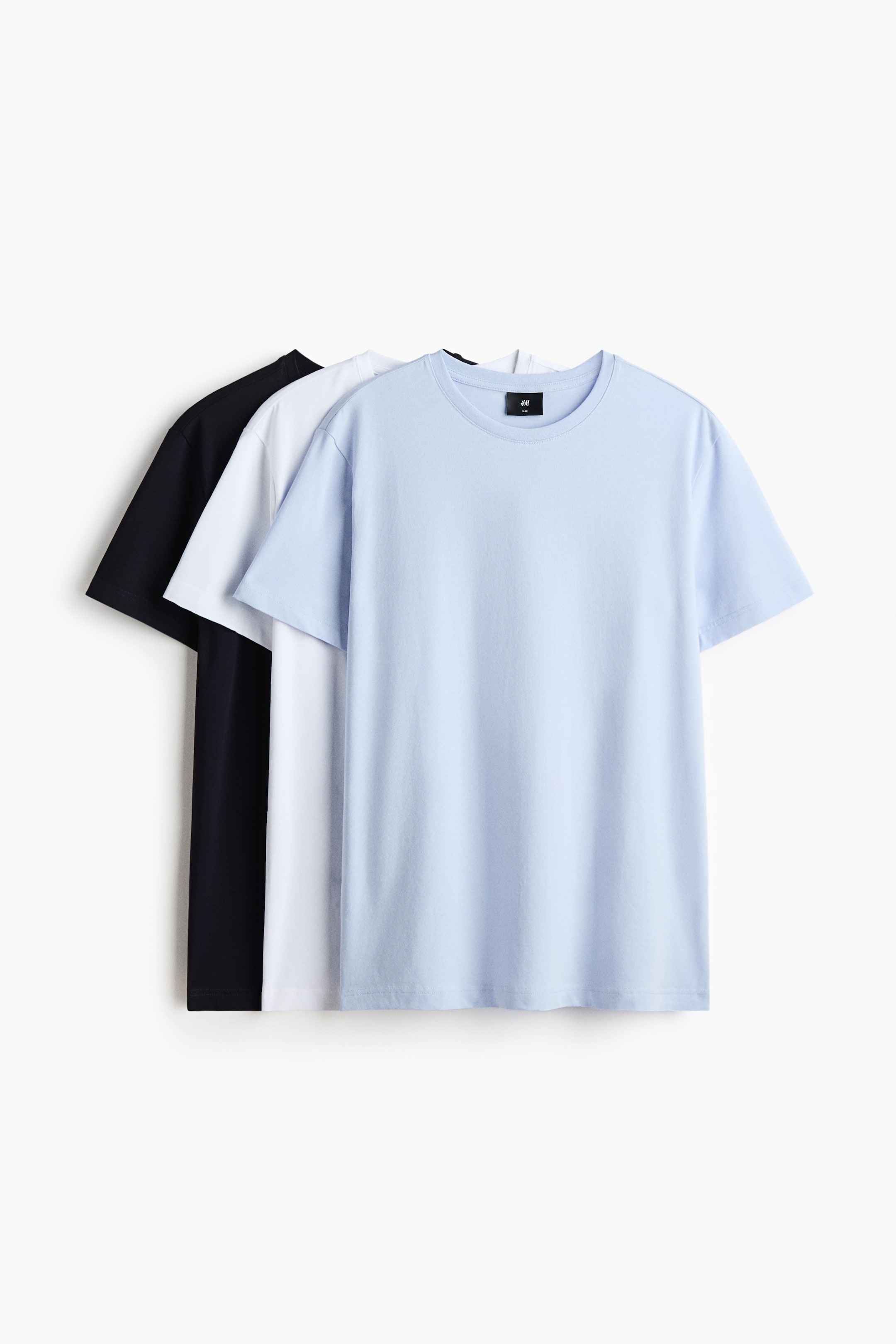 Agrandir l'image: Trois t-shirts sont présentés en superposition, de face : le t-shirt de devant est bleu clair, suivi d’un blanc, puis d’un noir. Chaque t-shirt présente une encolure ronde finition bord-côte, des manches courtes, un ourlet droit et une silhouette ajustée.
