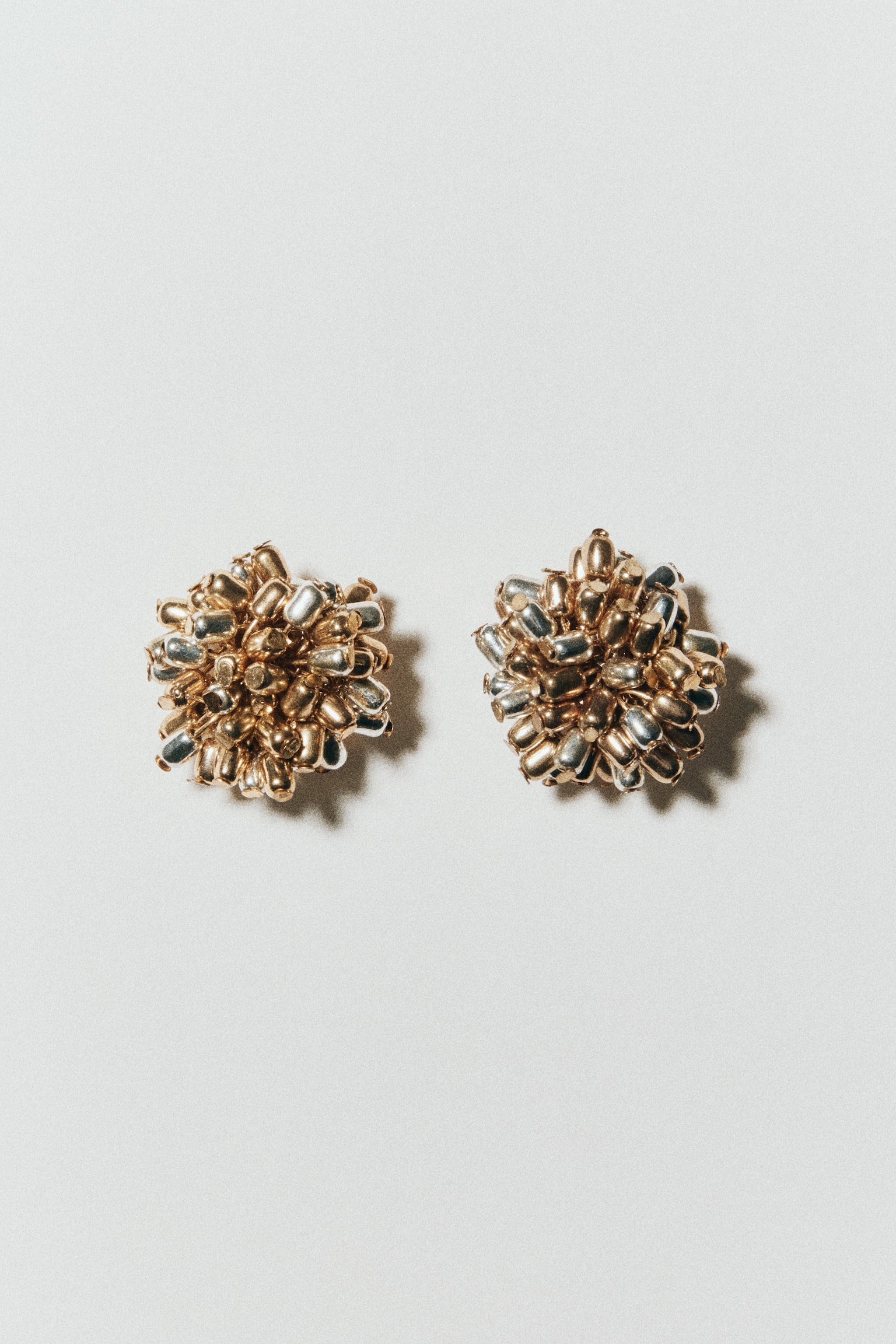 A pair of cluster stud earrings showcases a textured, rounded design made up of tightly clustered gold and silver metallic beads. The earrings are facing forward, highlighting their dimensional structure and mixed-metal finish. - 1