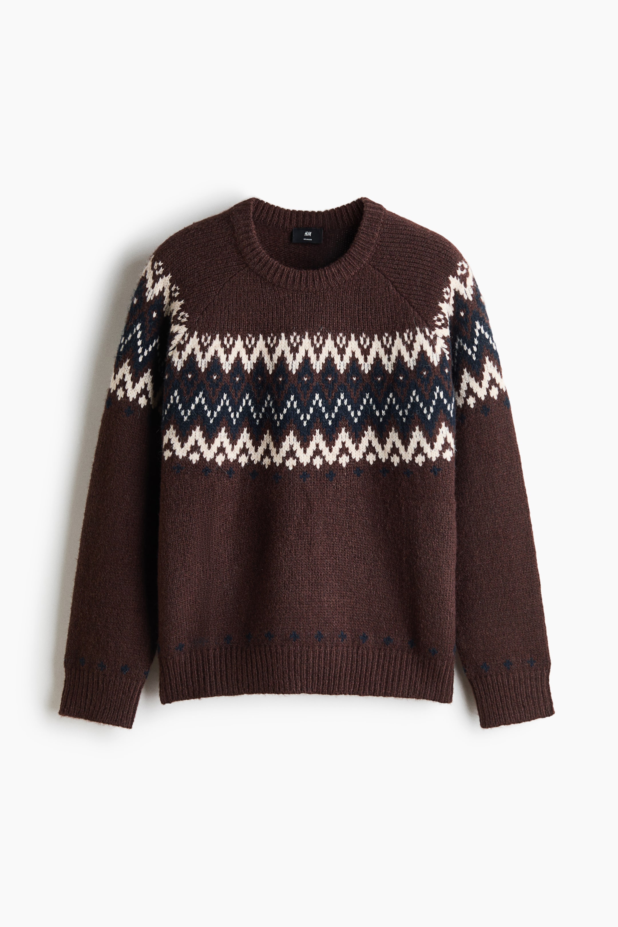 View larger image: A brown knit sweater showcases a Fair Isle-style geometric pattern in white and navy blue across the chest and upper sleeves. The sweater features a ribbed crew neck, long raglan sleeves with ribbed cuffs, and a ribbed hem.
