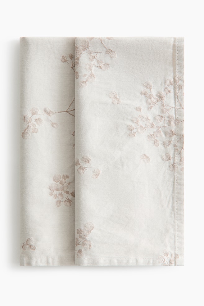 A folded off-white textile features a light brown embroidered botanical sprig pattern. It is neatly folded into a rectangular shape, displaying hemmed edges. - 1
