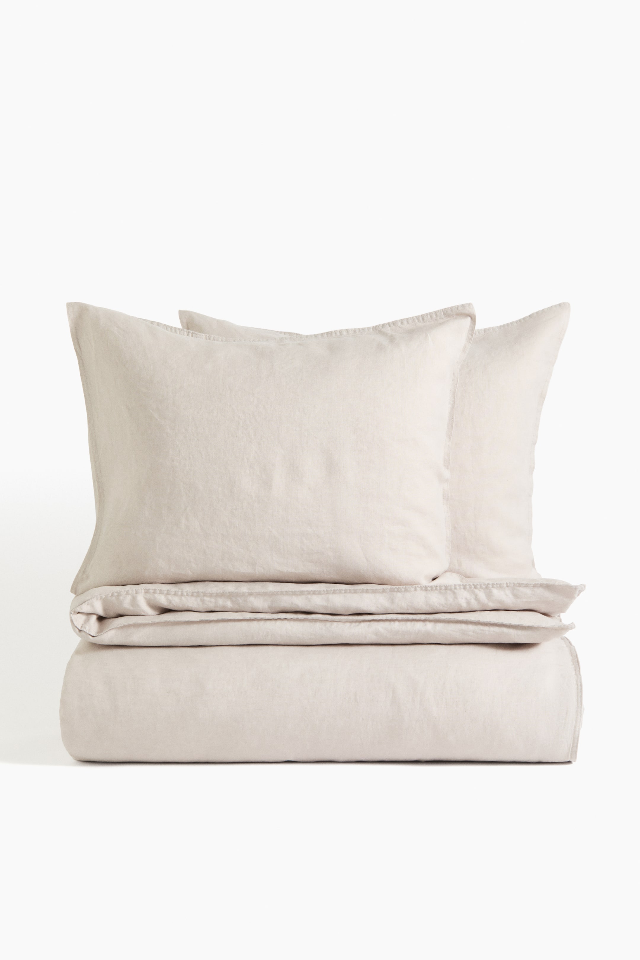 Ver imagem maior: Conjunto de capa de edredão duplo em tecido de linho de tom natural claro com uma textura lavada visível, apresentando uma capa de edredão dobrada com duas fronhas empilhadas no topo.