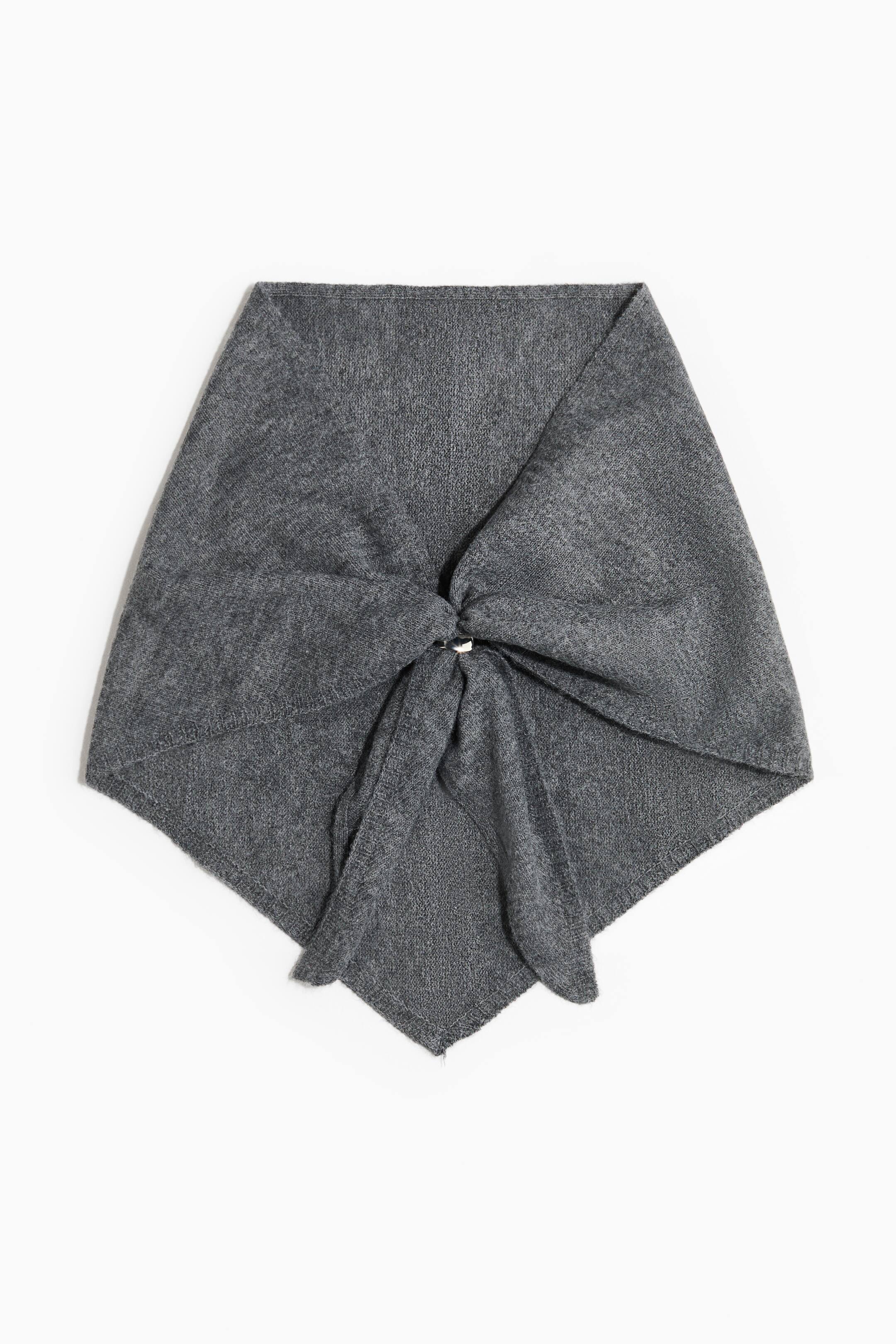 View larger image: A grey knit triangle scarf is facing front, showcasing a draped bandana-style design with a soft, fine-knit texture. The fabric is gathered at the centre with a knotted detail and tapers to a pointed bottom hem.
