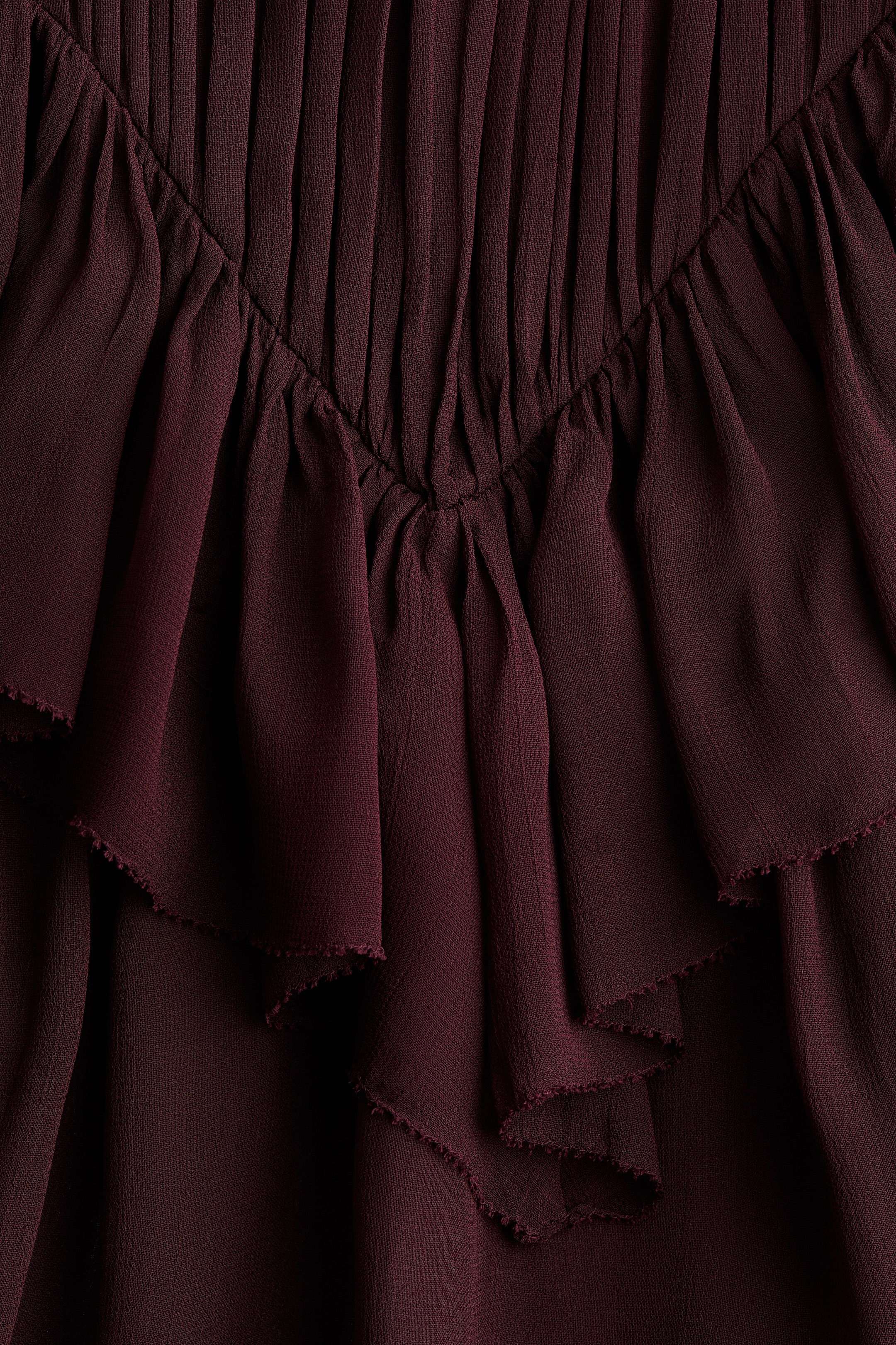View larger image: The sleeveless blouse is featuring a wide, V-shaped flounce at the front, made from a sheer viscose weave fabric. Pleats are gathering above the flounce, while its ruffled layers are displaying frayed edges.