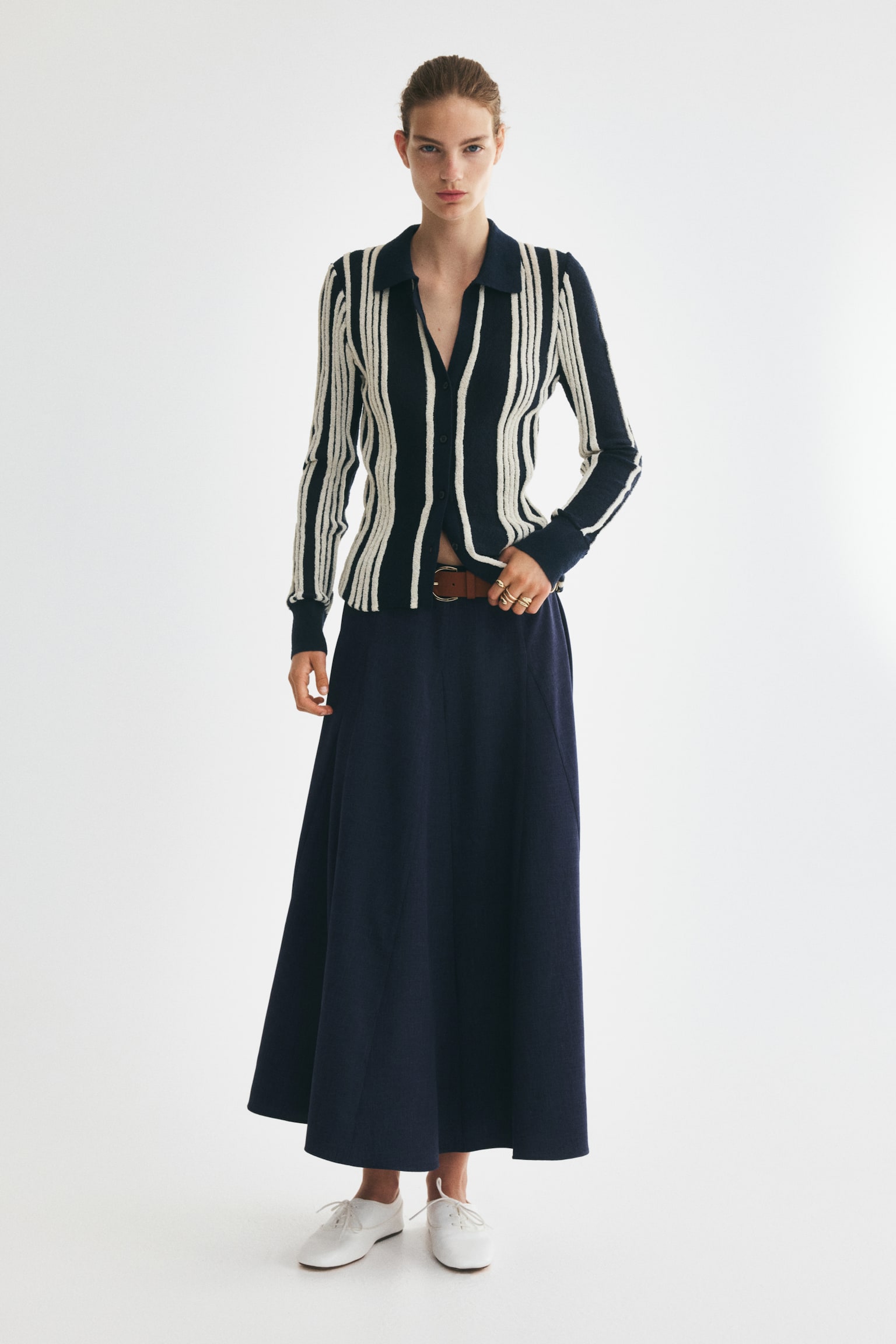 The dark blue textured midi skirt showcases a flared A-line silhouette with vertical seams. A brown belt with a silver-toned buckle is threaded through the waist. - 1