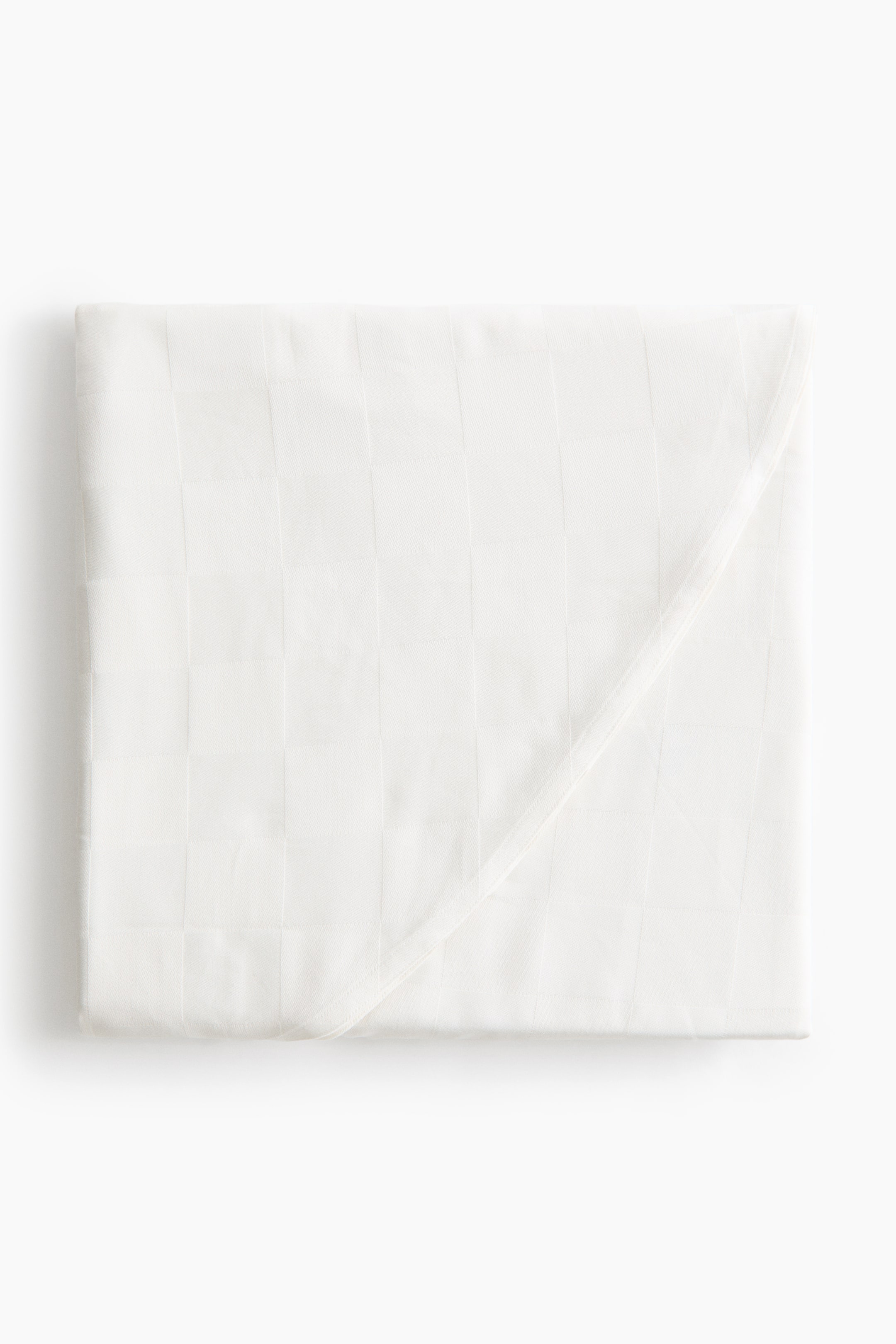 View larger image: A white hooded towel is folded into a square, showing a subtle woven grid pattern. A triangular corner section is folded diagonally across the front, highlighting a clean, hemmed edge.