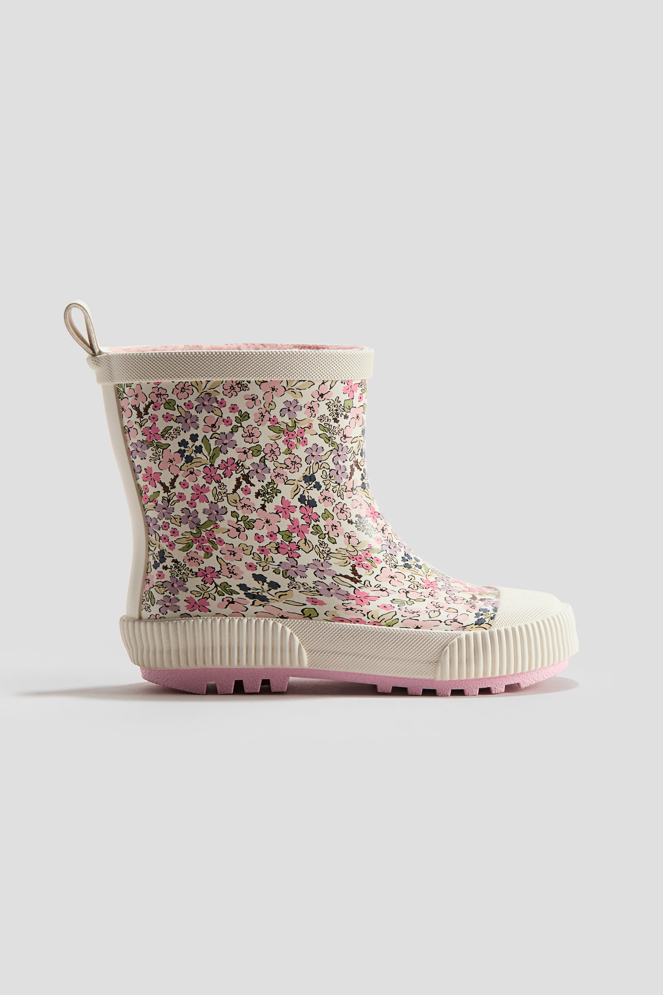Visa större bild: Wellingtons visar ett tätt blommönster i rosa, lila, grönt och blått på en ljus, krämfärgad botten. De är utformade med en krämfärgad, texturerad kant vid öppningen upptill, en dragögla baktill samt rejäla off-white-sulor med räfflade sidoväggar och en undersula i rosa med mönster.
