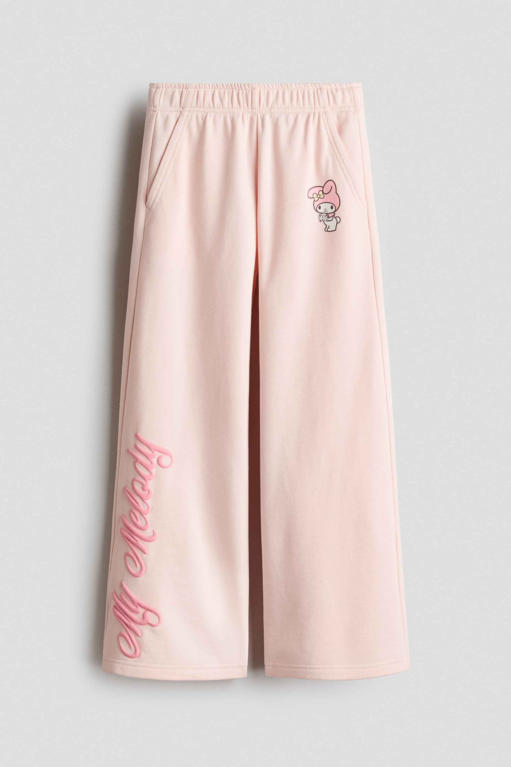 הצגת תמונה גדולה יותר: מכנסי ג'וגר ורודים מבד סווטשירט מוצגים מהחזית, עם גומי מכוסה במותניים, כיסים בצדדים ורגליים ישרות. הדפס של הדמות "מיי מלודי" מופיע על החלק העליון של רגל ימין, בעוד ש"מיי מלודי" רקום בכתב יד על החלק התחתון של רגל שמאל.