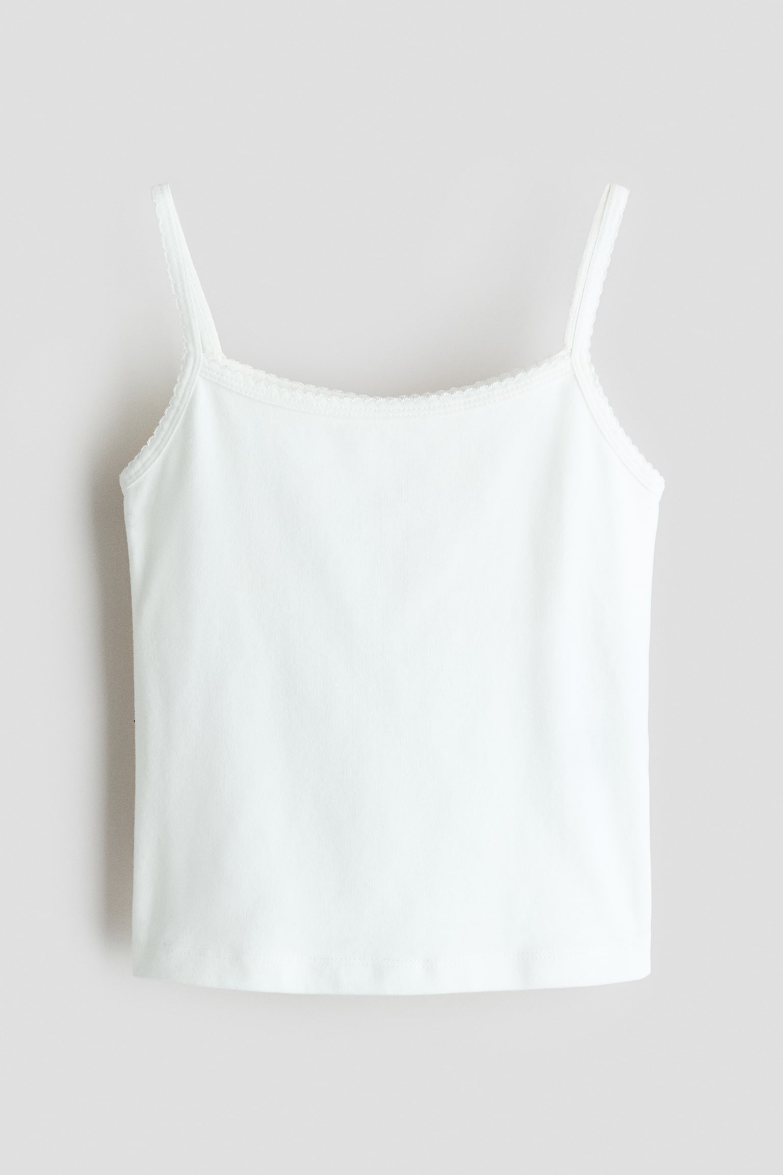 A white camisole is shown from the front, featuring thin shoulder straps and a straight neckline adorned with delicate lace trim. The sleeveless top presents a smooth texture with a straight hemline.