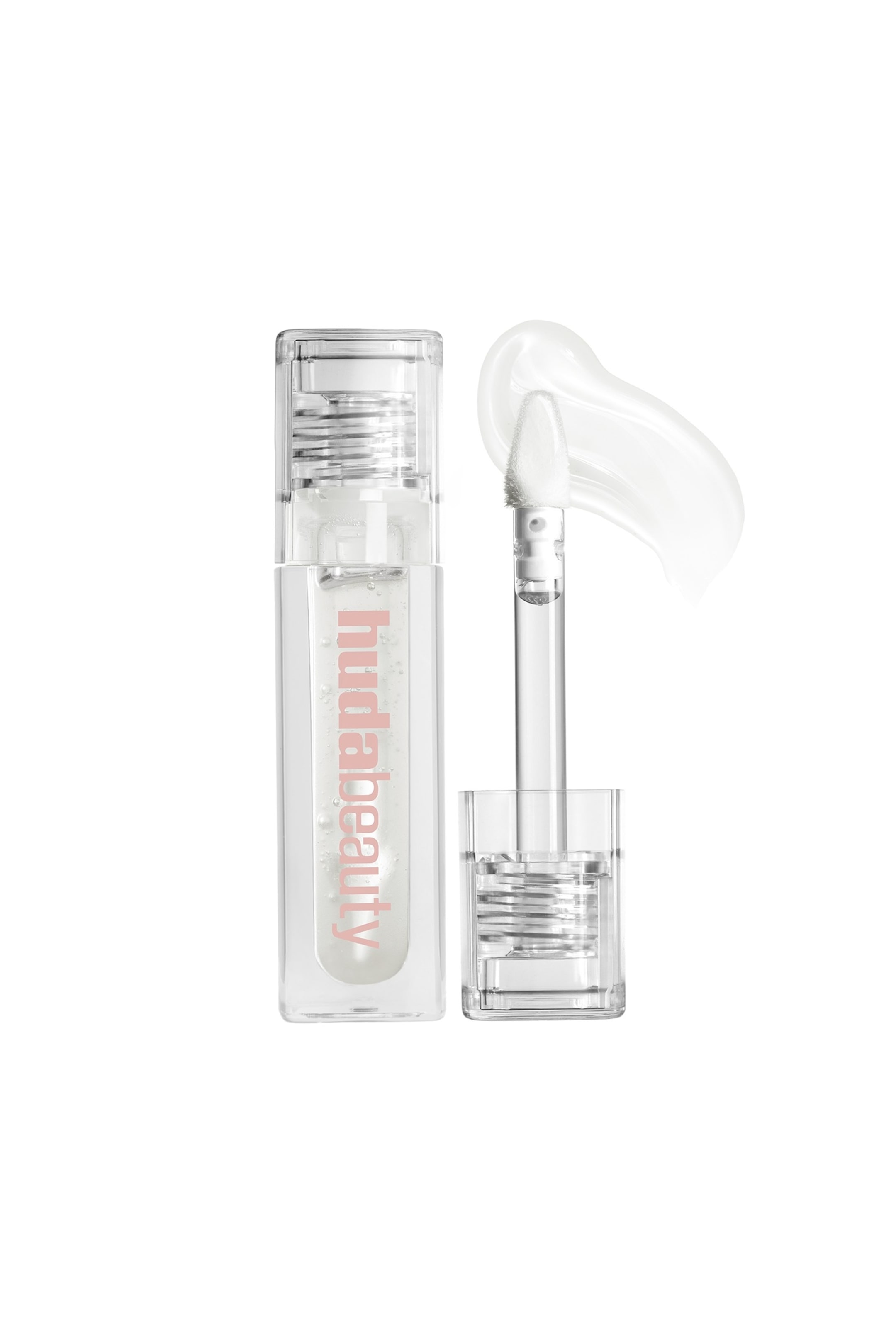 Vis større bilde: En Huda Beauty klar lipgloss presenteres med sin rektangulære, klare tube, med "hudabeauty" skrevet vertikalt i rosa. En klar applikatorstav med en hvit, avsmalnet, fluffy tupp står oppreist ved siden av tuben, og viser en påført dråpe av klar gloss.