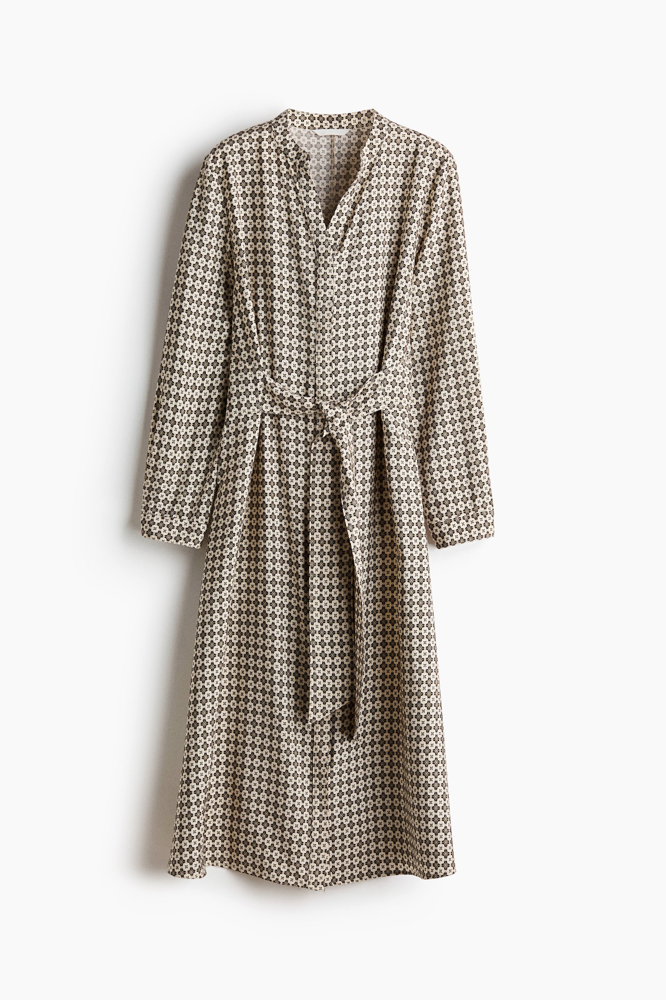 View larger image: A midi dress showcases a geometric pattern of dark brown shapes on a cream background, viewed from the front. It features a V-neck band collar, long sleeves, and a matching fabric tie belt that cinches the waist.