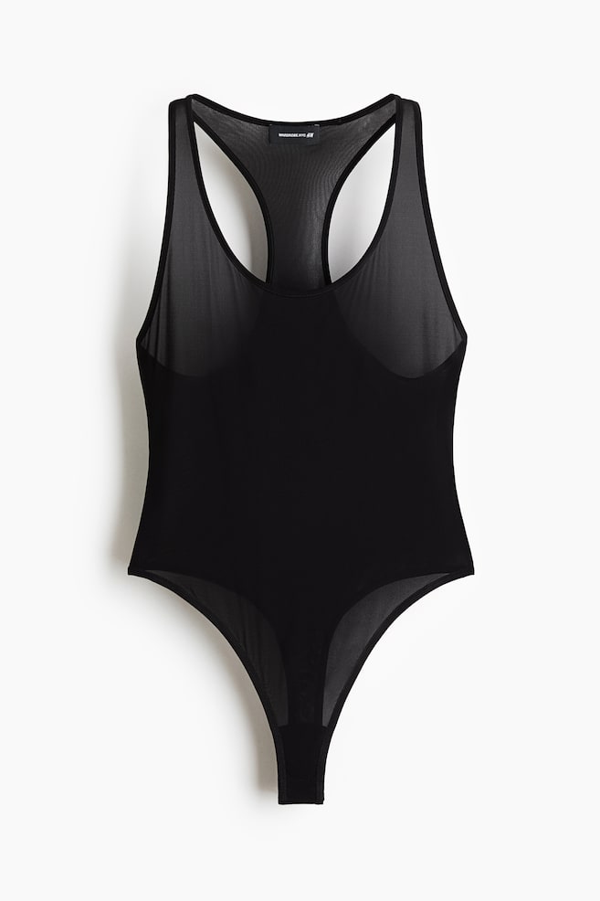 A black bodysuit is displayed front-facing, featuring a scoop neckline and a racerback design. The upper body, including the shoulders, is crafted from sheer black mesh, contrasting with the opaque black fabric of the torso and the sheer black mesh of the thong-style bottom. - 1