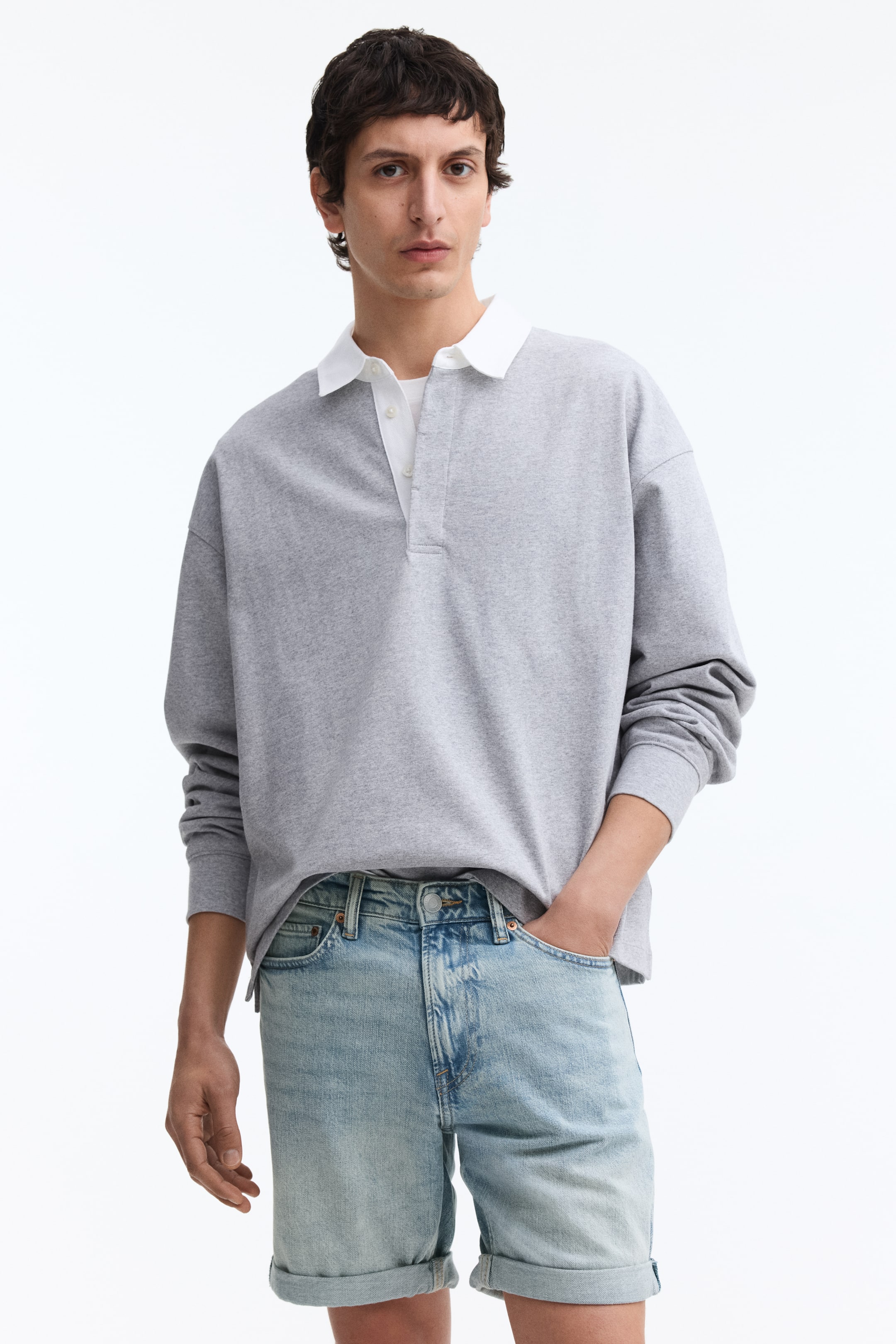 View larger image: A gray long-sleeved polo shirt is displayed from the front, showcasing a white contrasting collar, a partially open white button placket, and banded cuffs. A white undershirt is visible beneath the placket.