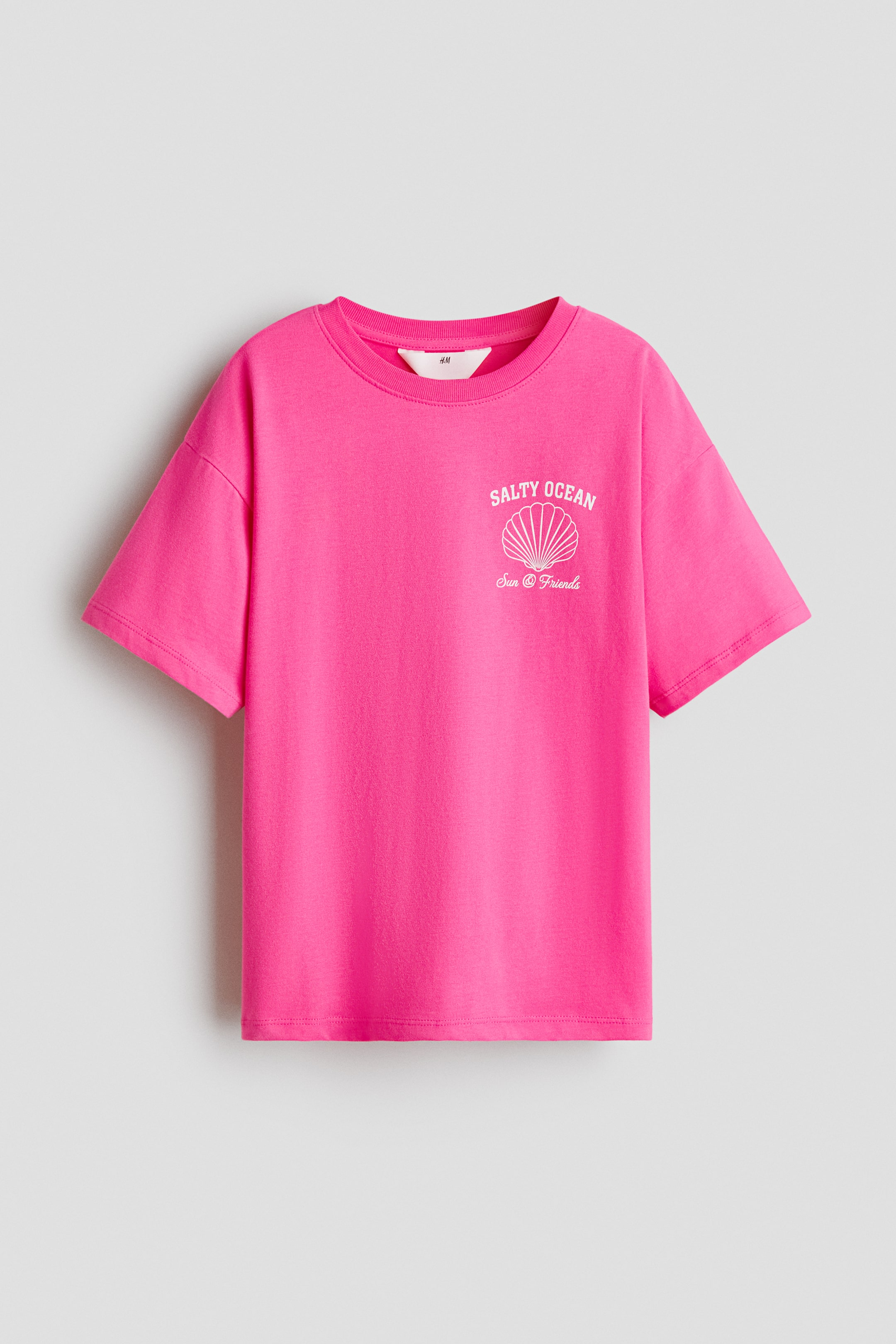 Größeres Bild anzeigen: Ein pinkfarbenes T-Shirt aus bedrucktem Baumwolljersey präsentiert seine Vorderseite, mit einem runden, gerippten Halsausschnitt und überschnittenen Schultern. Auf der linken Brustseite ist ein weißer Druck zu sehen, der den Text "SALTY OCEAN" über einer Muschel-Grafik und "Sun & Friends" darunter zeigt.