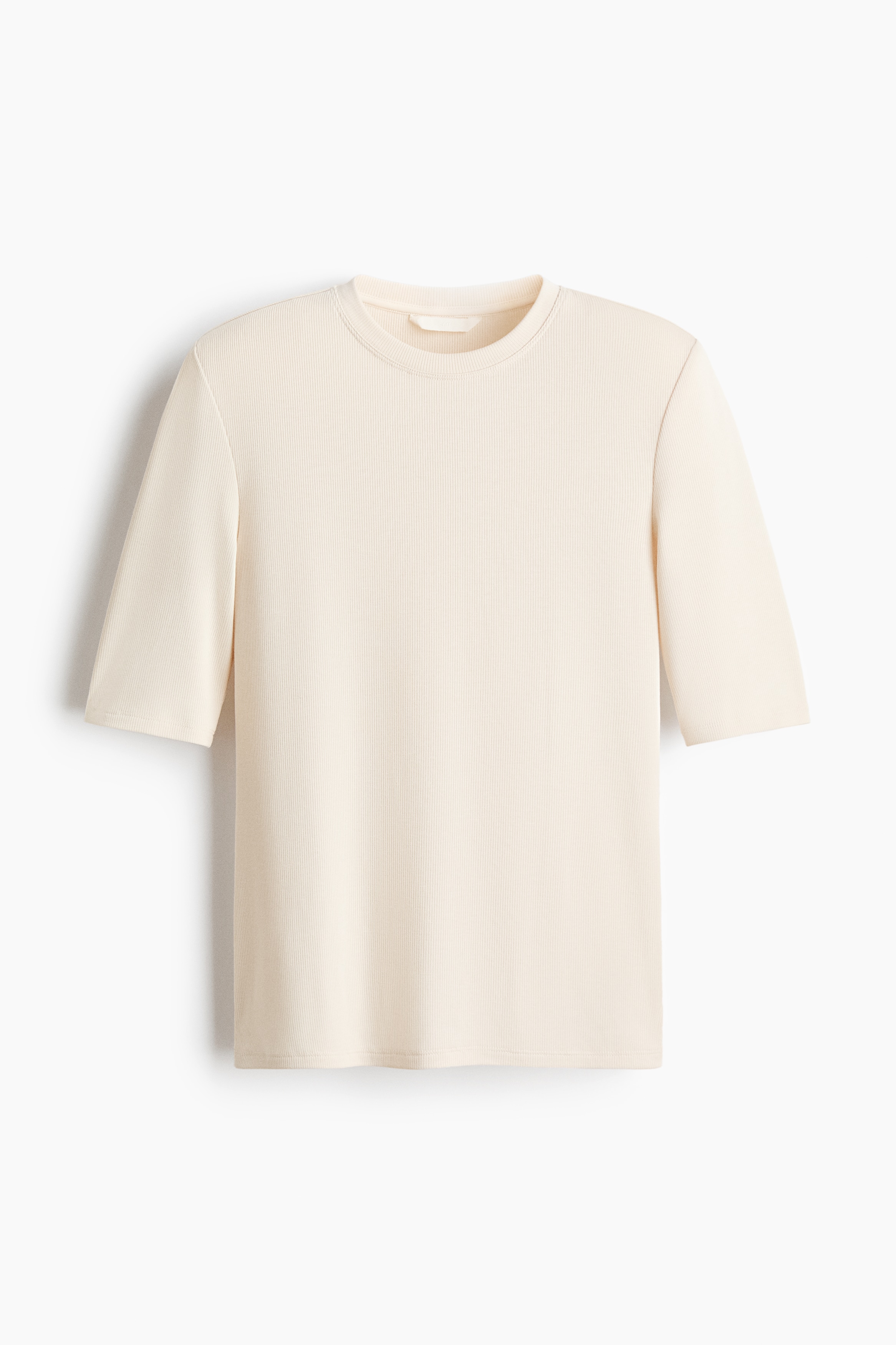 A fitted tee in ribbed jersey featuring a round neckline, structured shoulder pads, and a straight-cut hem is being worn by the model. The tee is styled with light-colored jeans, and the model is holding a small black drawstring bag.