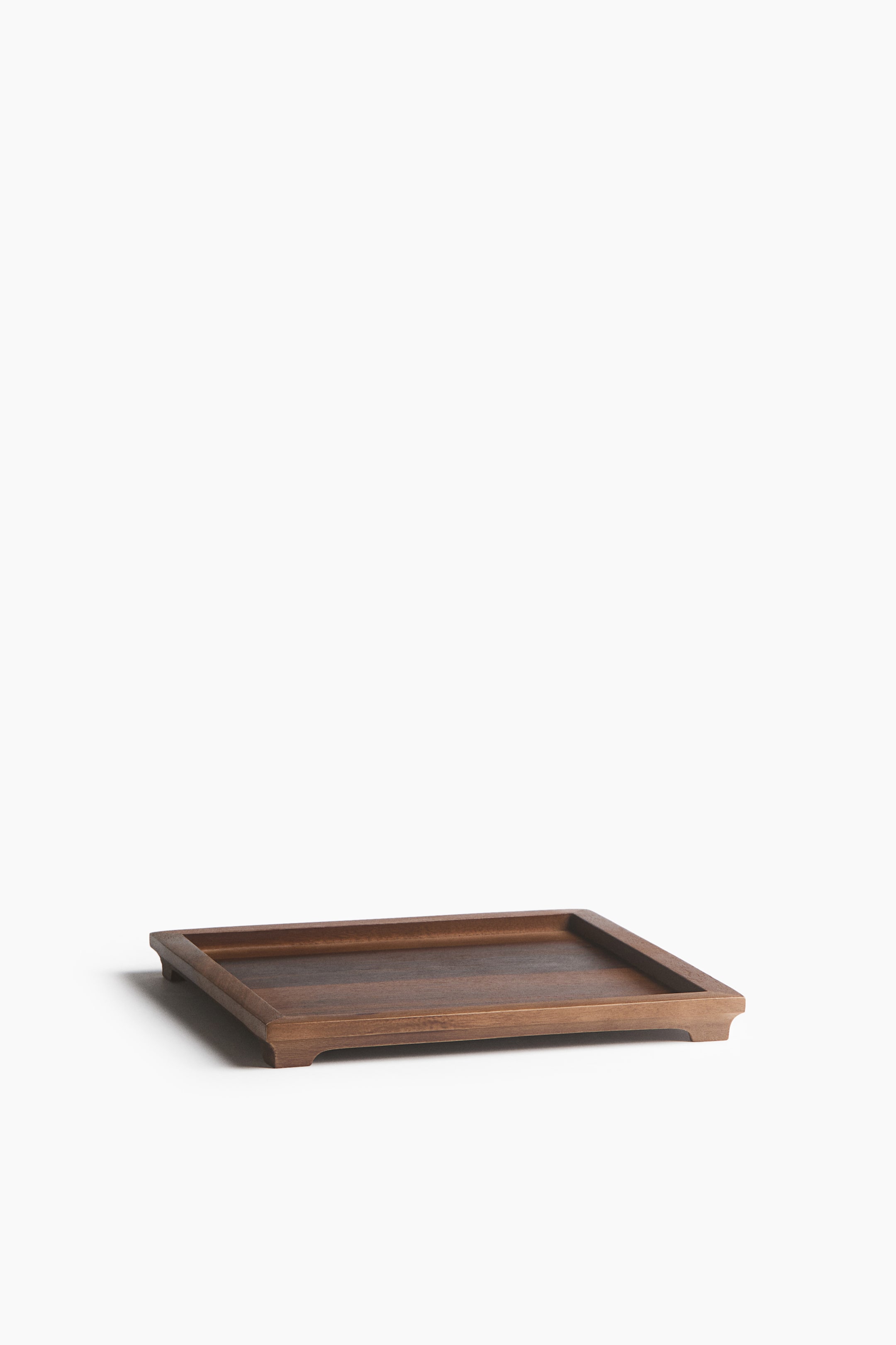 View larger image: A rectangular wooden tray is shown from a front three-quarter angle, highlighting its rich brown natural wood grain and raised outer edges. The tray rests on four small integrated corner feet that lift its base.