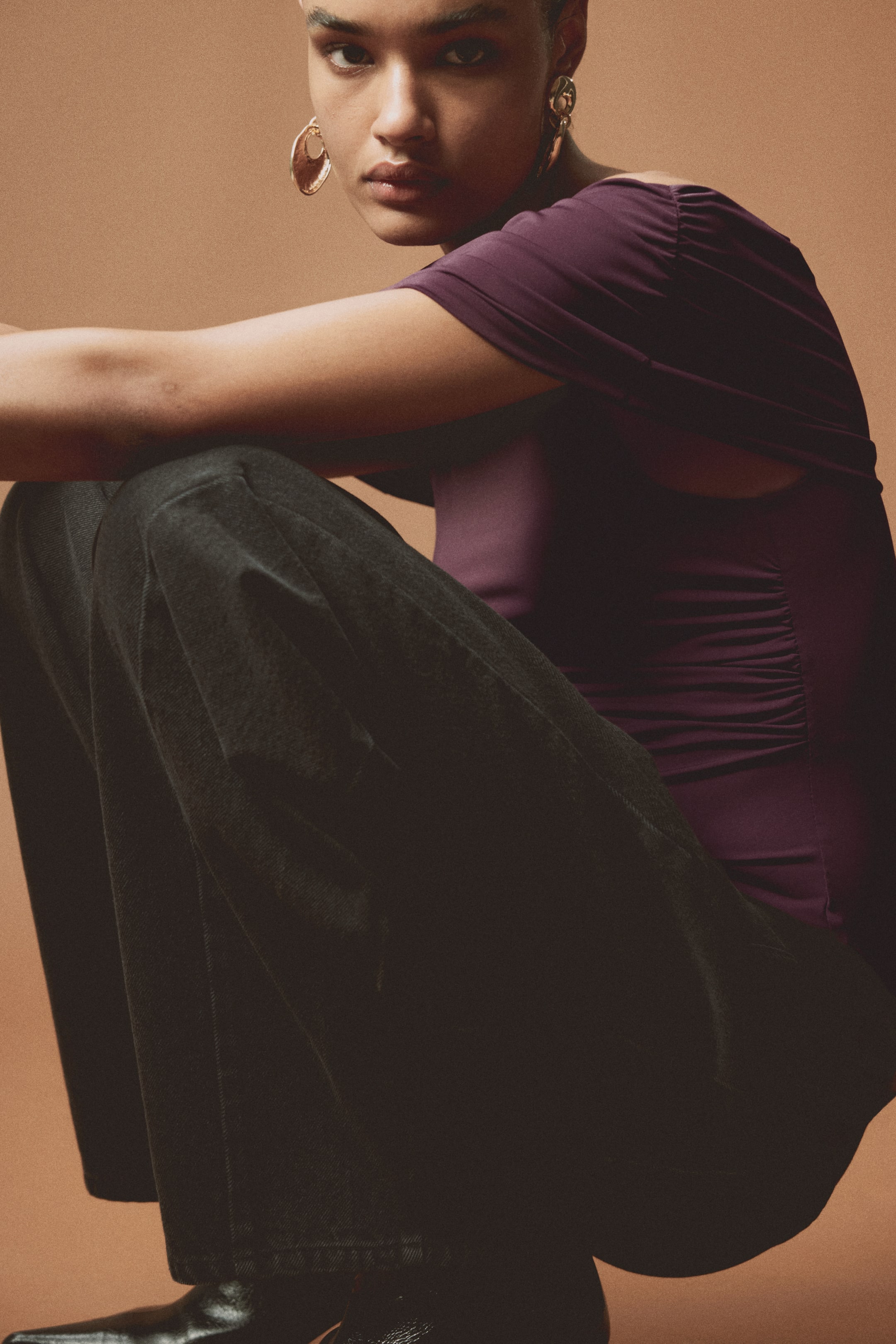View larger image: The model is wearing a fitted, dark purple off-the-shoulder top crafted from stretch jersey. It boasts gathered seams that create a draped effect, complemented by a wide, asymmetric foldover at the top, forming a stylish one-shoulder silhouette.