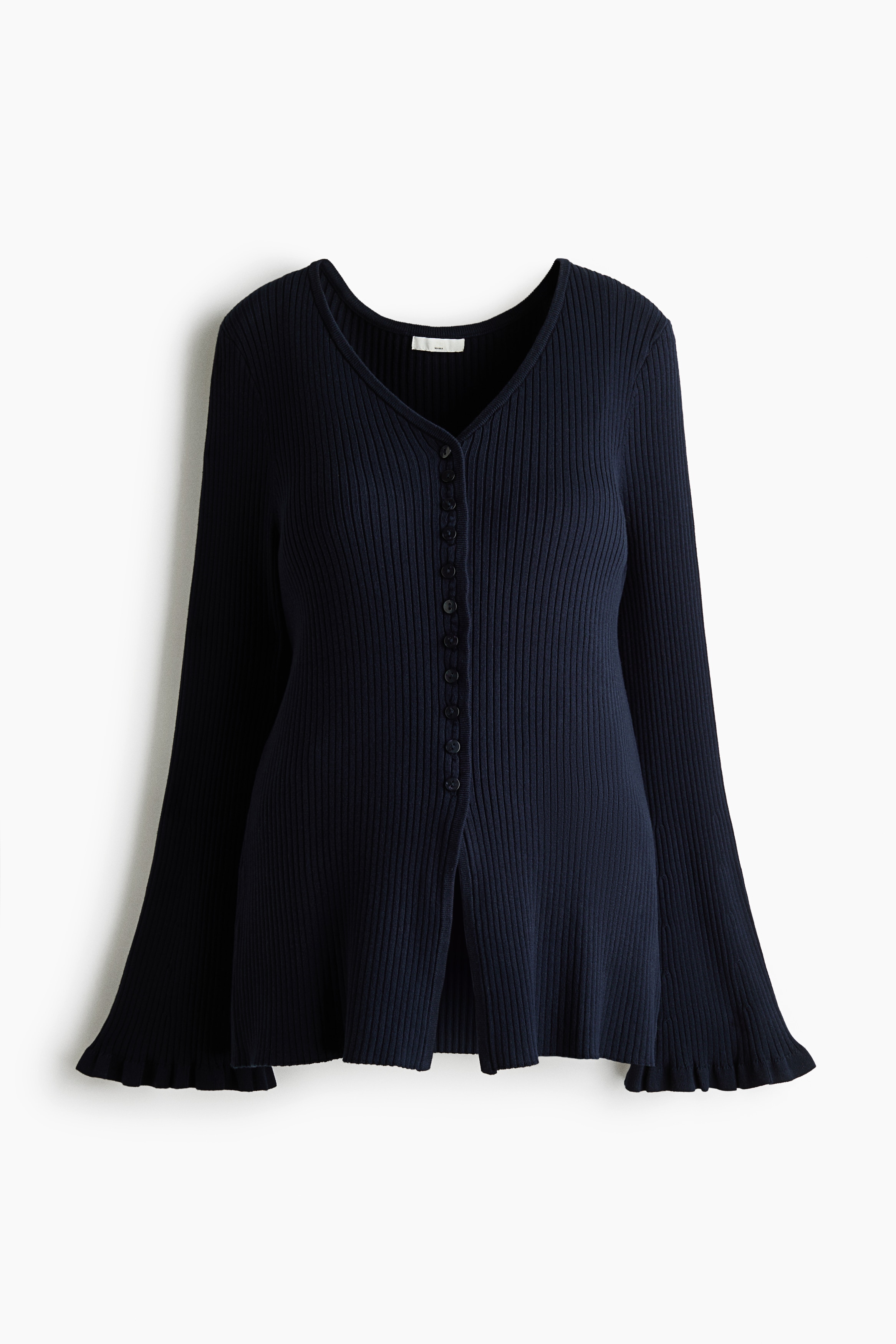 A long, fitted, dark blue rib-knit cardigan is worn by the model, featuring a V-neckline, front button fastening, and gently flared sleeves with frill-trimmed cuffs. The cardigan is styled with matching dark blue rib-knit trousers.