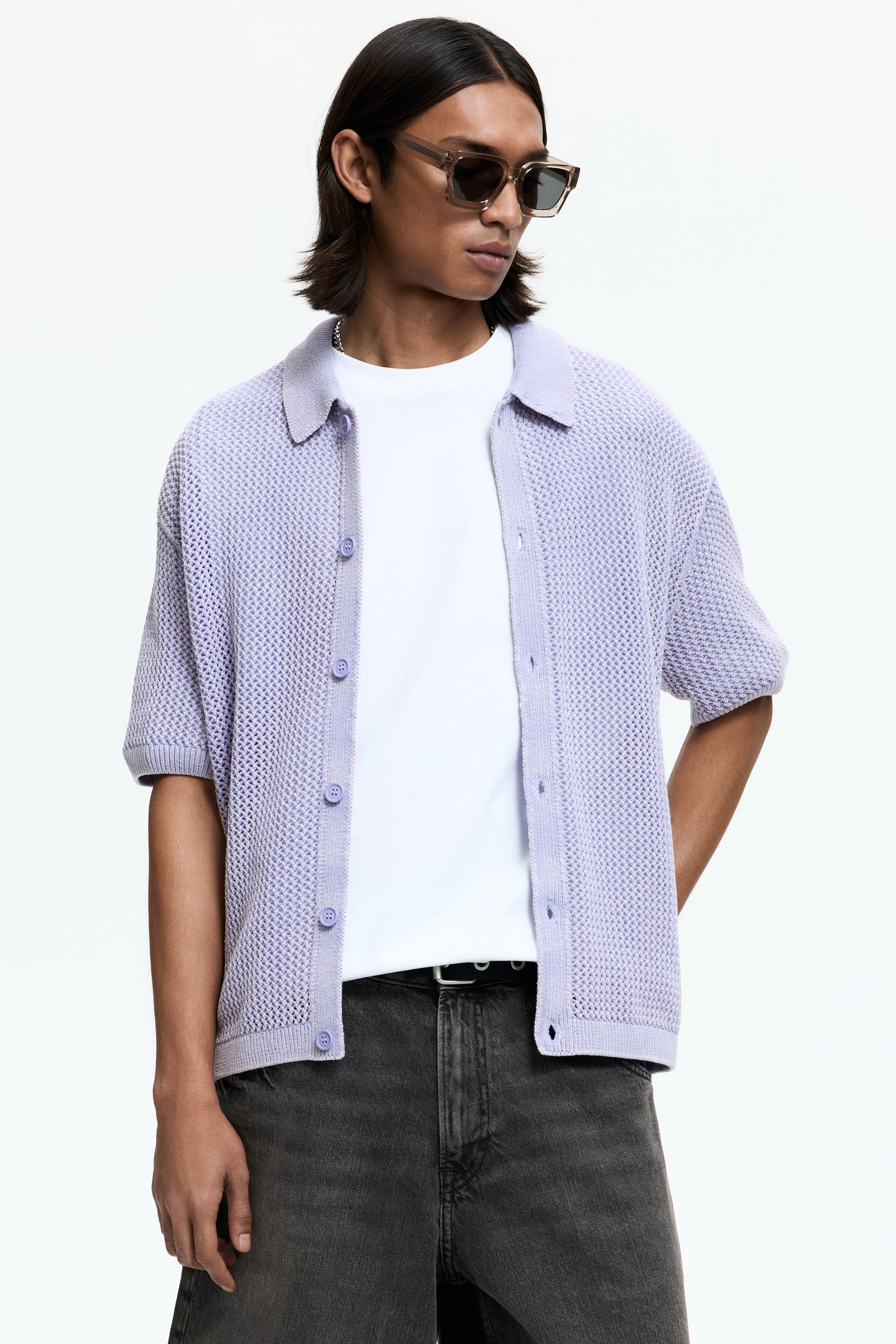 View larger image: A lavender open-knit short-sleeved shirt is showcased from a slight right-facing angle, featuring a spread collar, ribbed cuffs, and a ribbed hem. It displays a button-up front with six lavender buttons along the placket and is styled open over a white crewneck t-shirt.