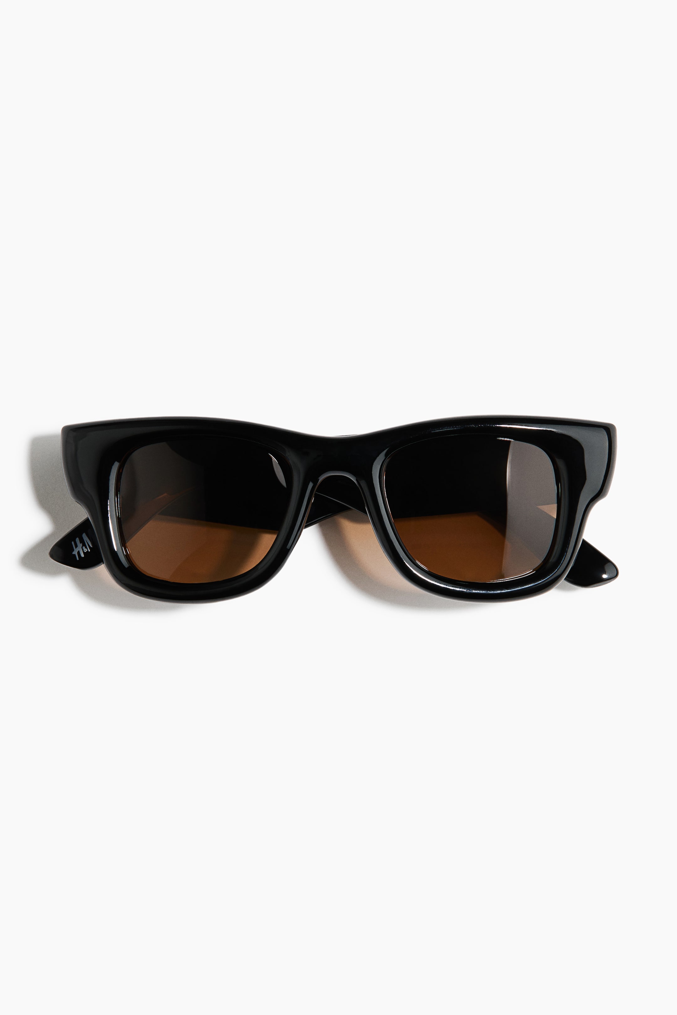 View larger image: The sunglasses feature a black, glossy rectangular frame with slightly curved edges and brown-tinted lenses. A small "H&M" logo is visible on the left temple arm.