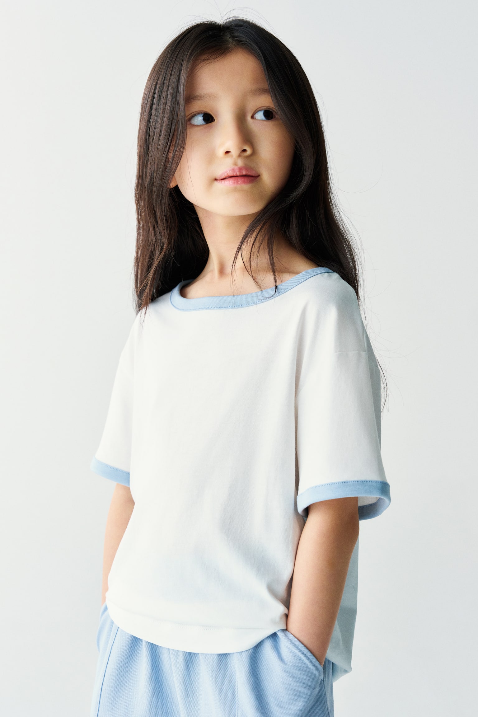 The model is wearing a white short-sleeved ringer t-shirt with light blue trim on the collar and cuffs, paired with matching light blue shorts. - 1