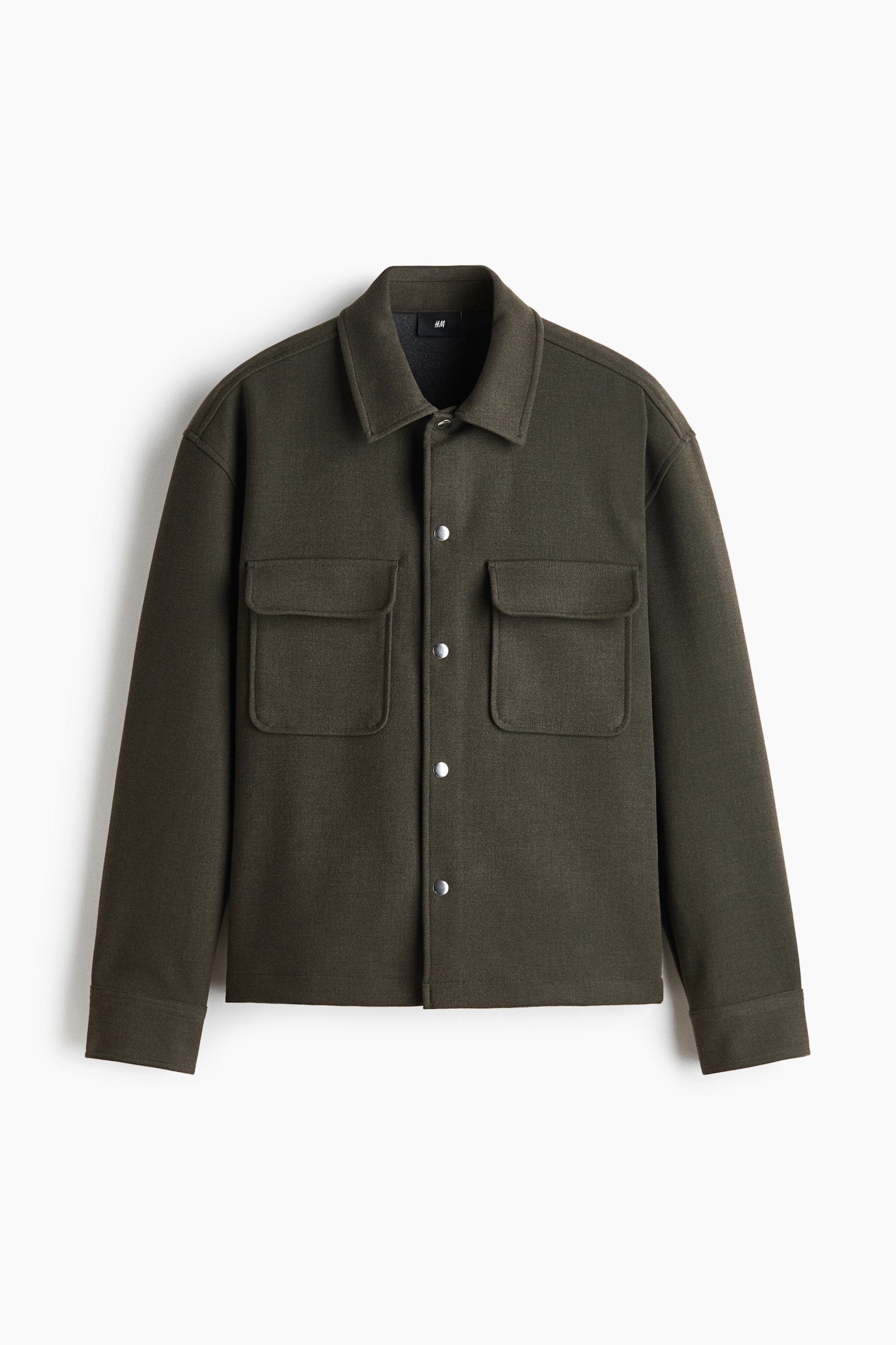 Una giacca-camicia verde oliva scuro Ã¨ mostrata frontalmente, con una vestibilitÃ  strutturata e squadrata, colletto a punta e chiusura frontale con bottoni automatici argentati. Presenta due ampie tasche applicate sul petto con patta e maniche lunghe con polsini rifiniti in modo pulito.