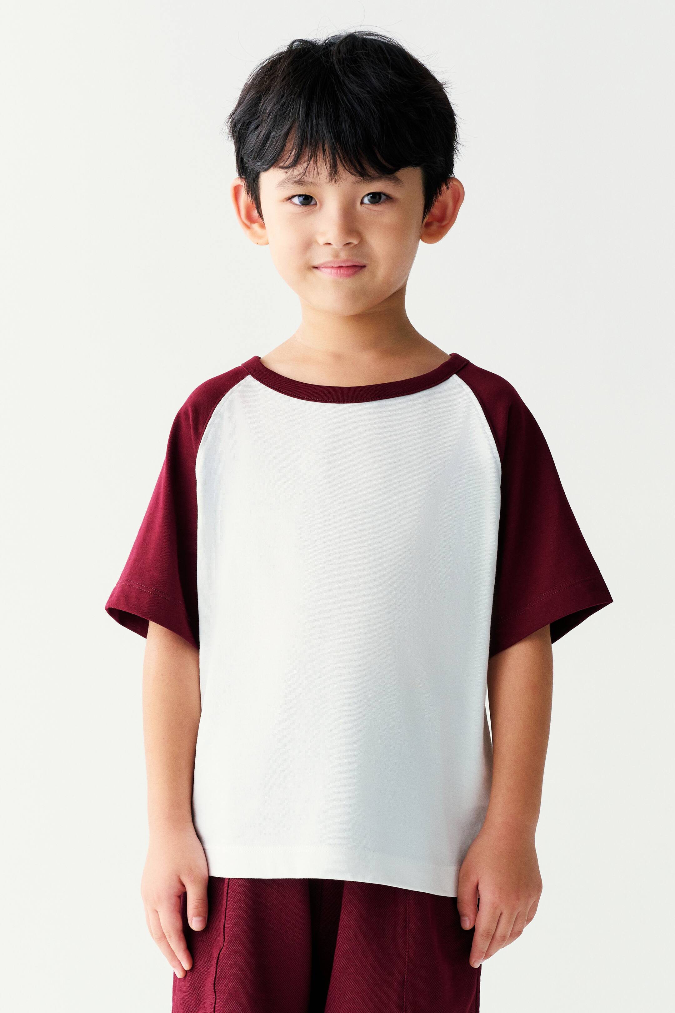 View larger image: A short-sleeved raglan T-shirt featuring a white body, burgundy sleeves, and a matching burgundy crew neck is being worn by the model. The T-shirt is paired with matching burgundy shorts.