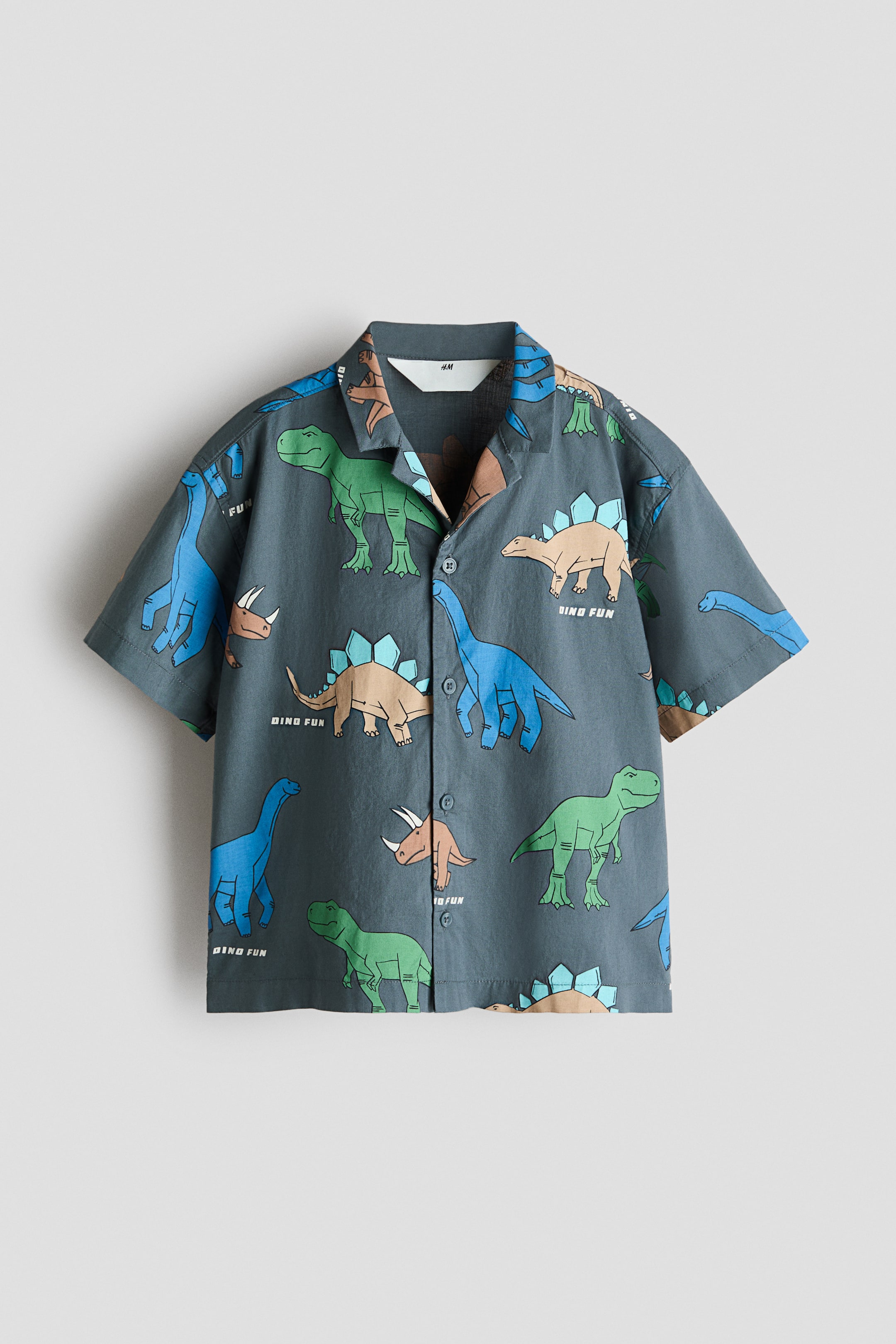 View larger image: A front-facing, short-sleeved dark gray shirt showcases a print of blue, green, and brown dinosaurs with the text "DINO FUN." It features a revere collar and a full button-front closure with matching dark buttons.