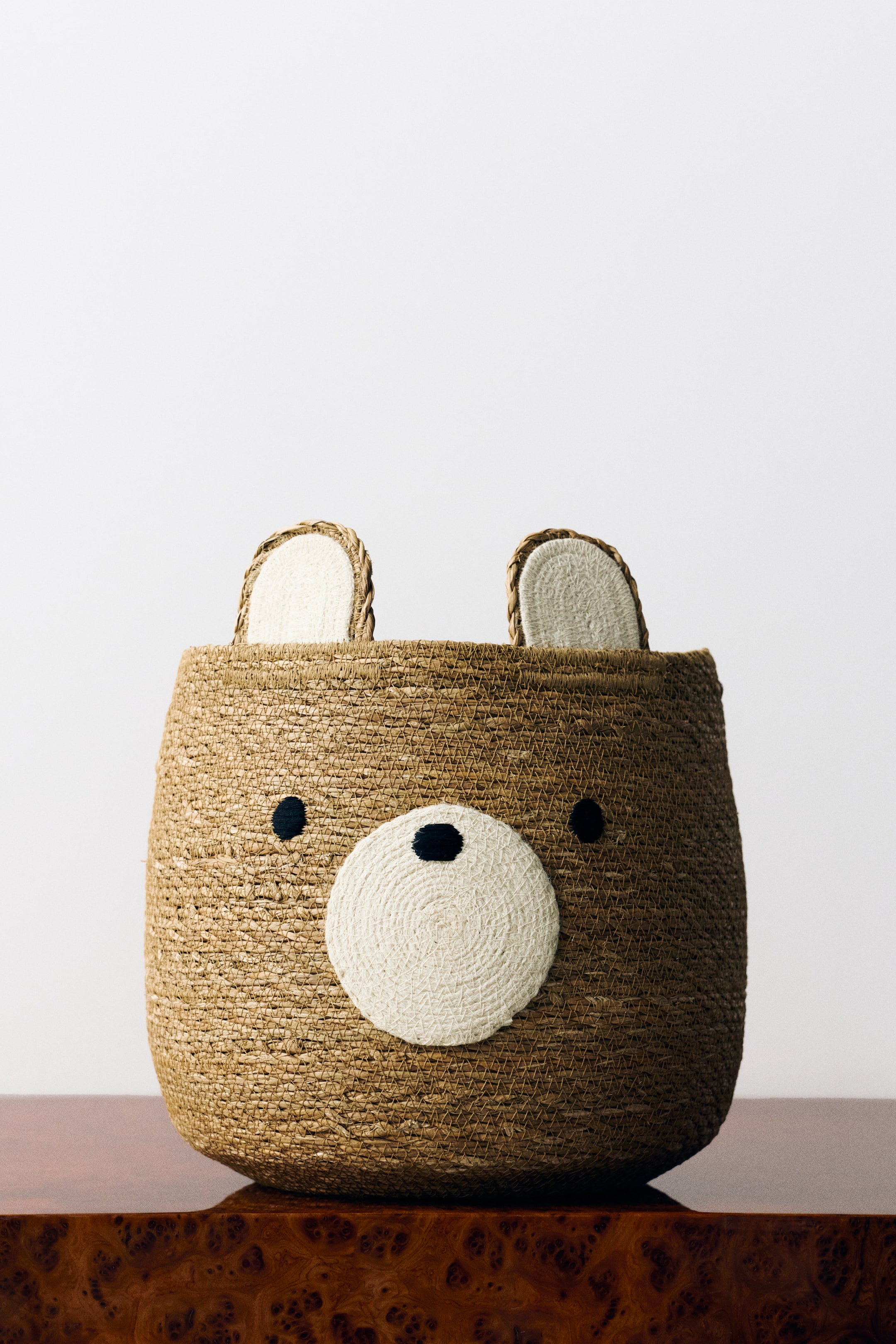 View larger image: A front-facing view shows a large, rounded bear-shaped storage basket woven from textured brown jute. The basket features two upright ears lined with cream-coloured coiled rope, embroidered black eyes, and a circular cream snout with a small black nose.