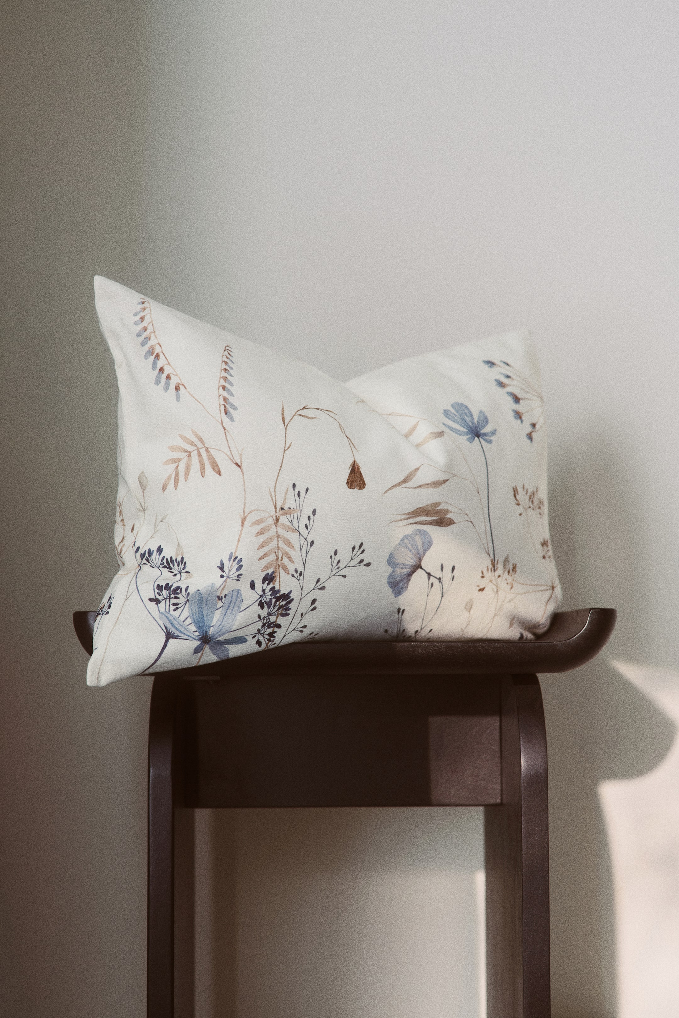 Größeres Bild ansehen: Ein rechteckiger Kissenbezug aus Baumwoll-Canvas zeigt auf seiner Vorderseite einen botanischen Druck. Der Druck besteht aus zarten hellblauen und gedämpften braunen Blumen- und Blattmotiven, die auf einem cremeweißen Hintergrund platziert sind.