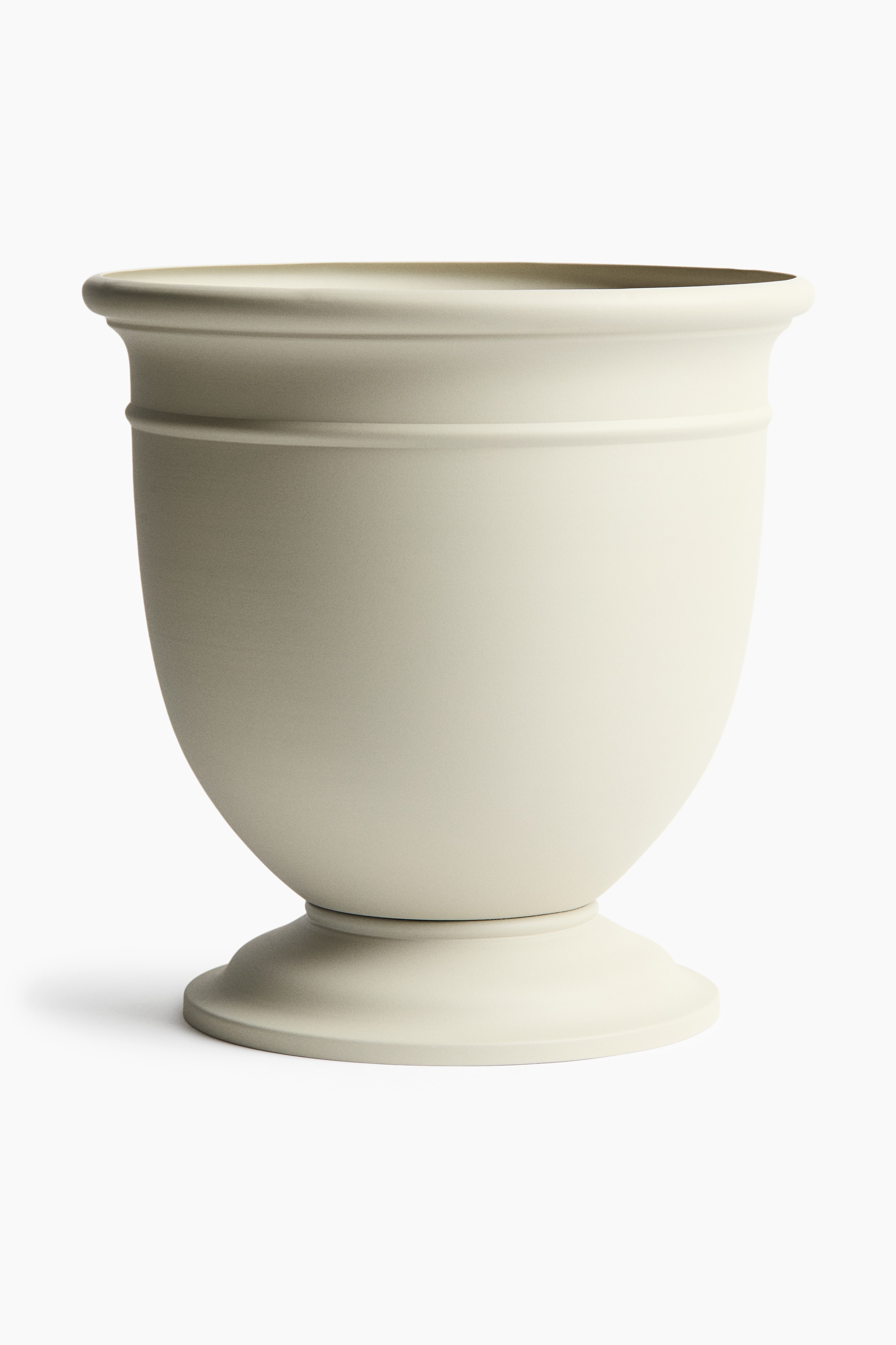 Une plante d'agave vert foncé, avec des feuilles épaisses et pointues rayonnant vers l'extérieur, aux bords tranchants et aux extrémités acérées, remplit un pot en forme d'urne de couleur beige clair. Le pot présente deux bandes horizontales en relief et repose sur une base à piédestal évasée.